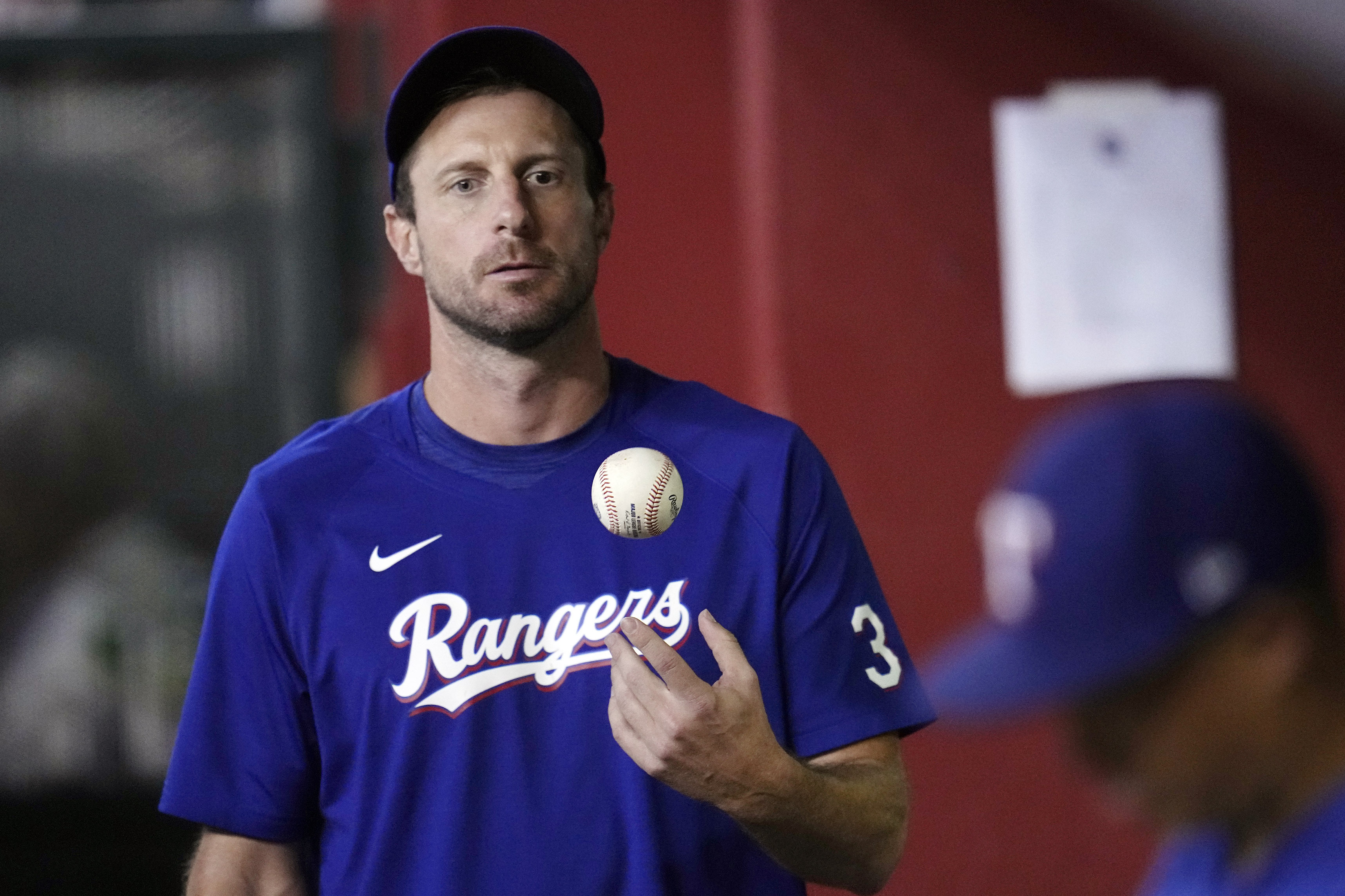 FILE- Texas Rangers' Max Scherzer flips the ball in the air as he paces the dugout during the seventh inning of a baseball game against the Arizona Diamondbacks Tuesday, Aug. 22, 2023, in Phoenix. Scherzer logged at least 179 innings in 10 of his first 16 years in the majors. And the three-time Cy Young Award winner learned some tough lessons on the road to pitching deep into games. That's one reason why the Rangers right-hander thinks Major League Baseball needs to look a lot deeper than a roster limit if it wants to return starting pitching to prominence. 