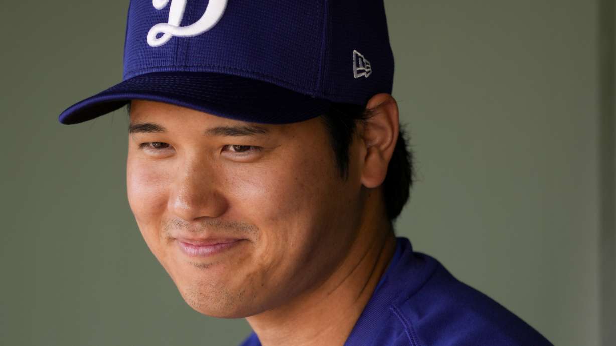 Los Angeles Dodgers designated hitter Shohei Ohtani smiles in the dugout before a spring training baseball game against the Texas Rangers, Wednesday, Feb. 28, 2024, in Surprise, Ariz.