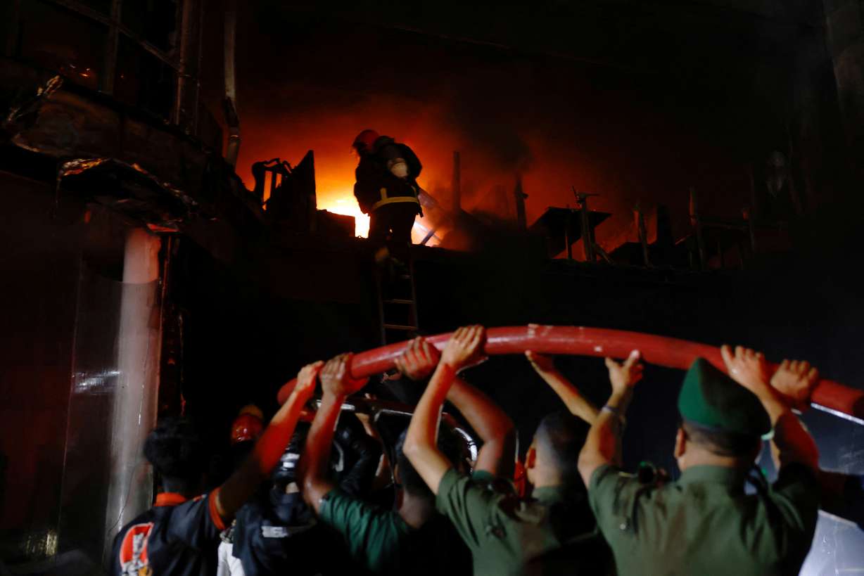Volunteers carry a water pipe as firefighters spray water to douse the fire after a fire that broke out in a multi-story building in Dhaka, Bangladesh, Thursday.