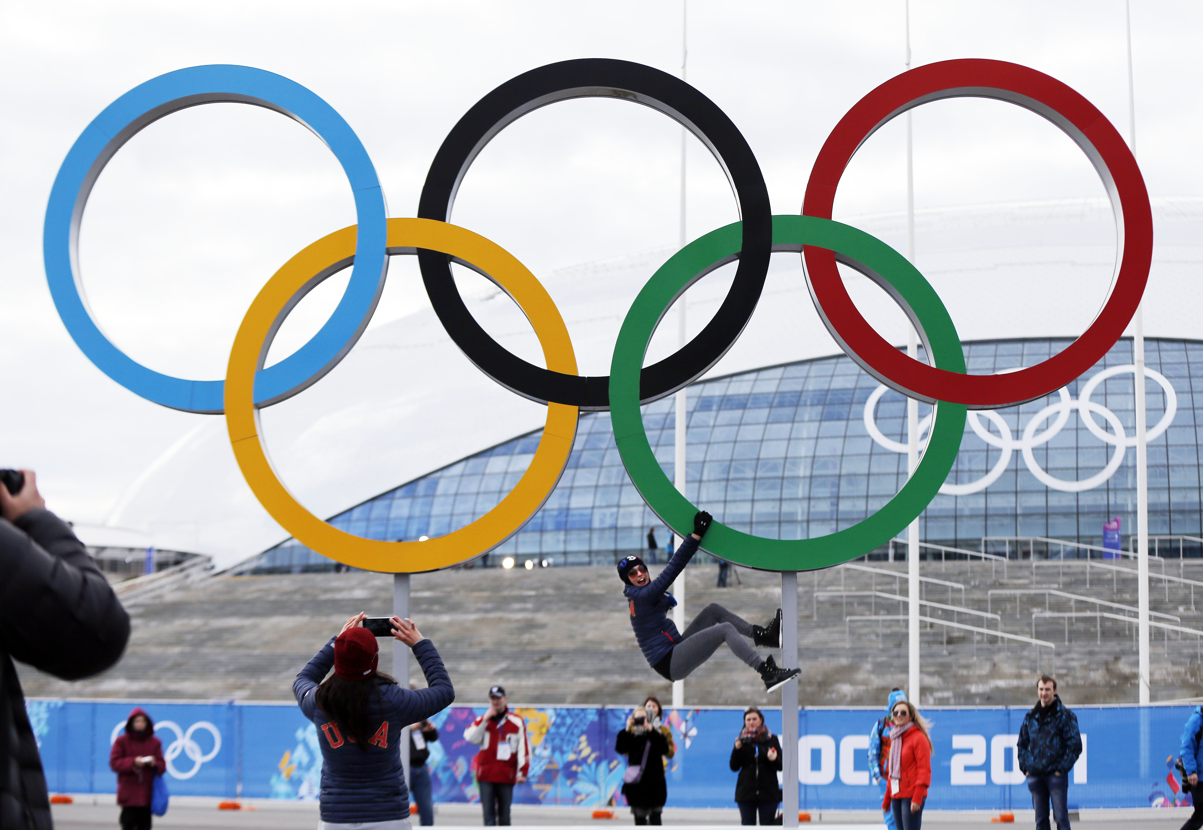 FILE - A participant hangs from the Olympic rings while posing for a teammate at Olympic Park ahead of the 2014 Winter Olympics, Wednesday, Feb. 5, 2014, in Sochi, Russia. A commission charged with reviewing the Olympic system in the United States recommended in a report Friday, March 1, 2024, that Congress rework key facets of the U.S. Center for SafeSport, including making it completely independent of the U.S. Olympic and Paralympic Committee and reimagining the way it deals with cases in the grassroots.