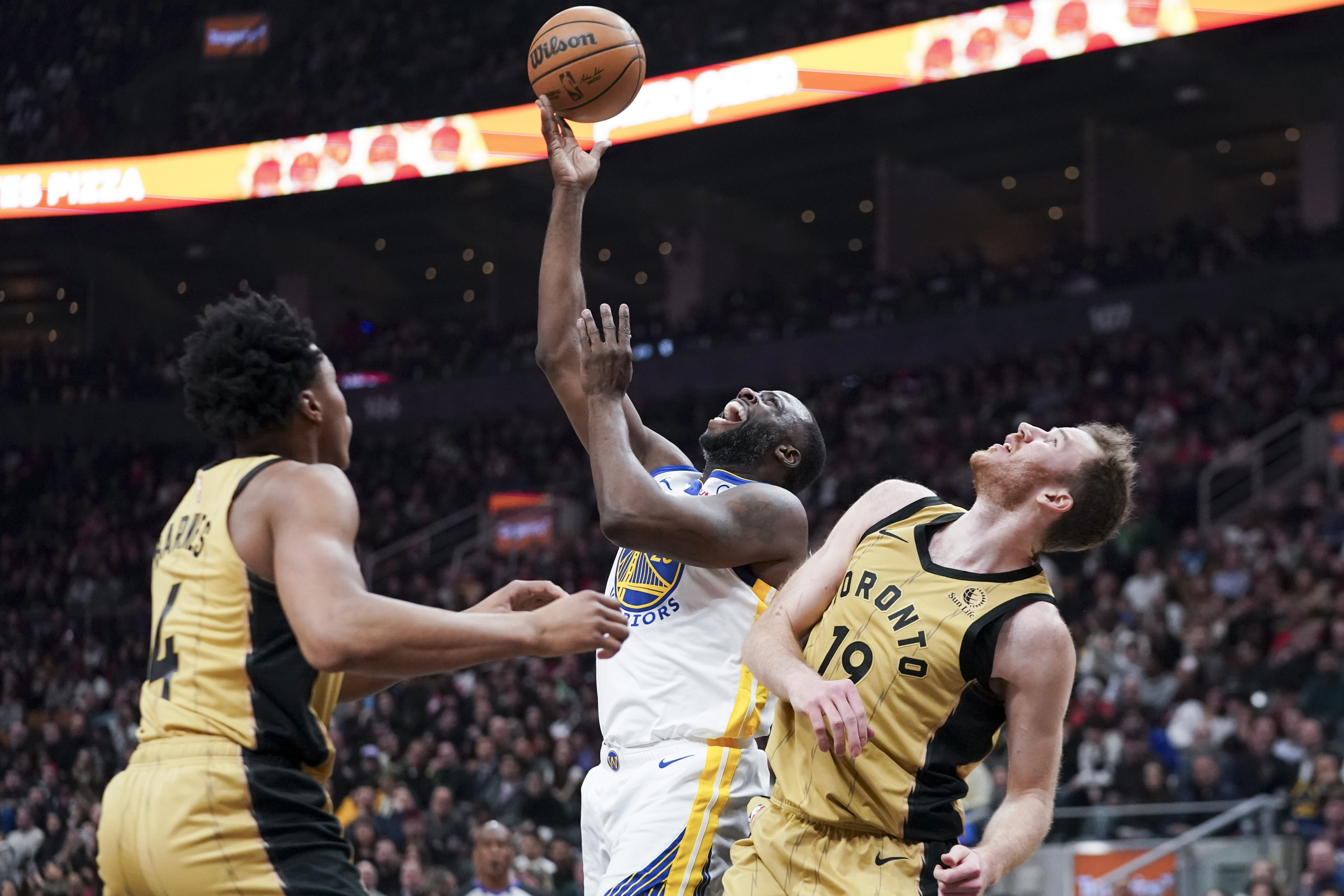 Golden State Warriors forward Draymond Green (23) jumps with the ball while being guarded by Toronto Raptors center Jakob Poeltl, right, and forward Scottie Barnes (4) during the first half of an NBA basketball game Friday, March 1, 2024, in Toronto.