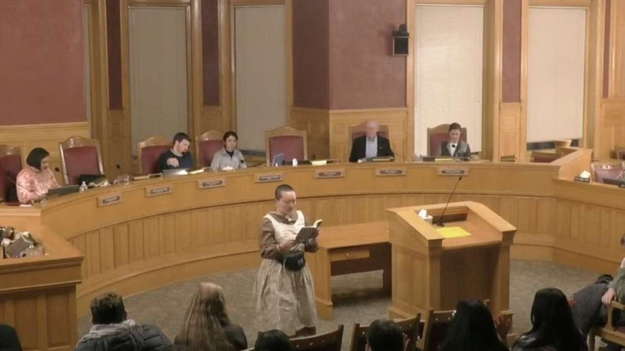 A protester reads from a book while the Salt Lake City Council attempts to resume a meeting Tuesday night. The meeting was delayed nearly 30 minutes by disruptions from a group opposed to the council's new public comment policy.