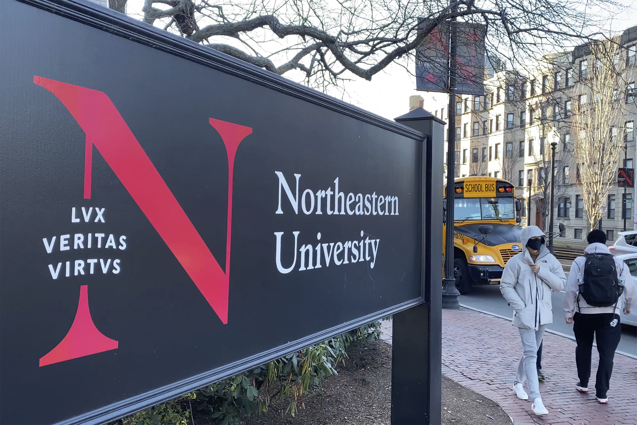 FILE - Pedestrians walk near a Northeastern University sign on the school's campus, Jan. 31, 2019, in Boston. Steve Waithe, a former college track and field coach at the university, could face seven years behind bars for setting up sham social media and email accounts in an attempt to trick women into sending him nude or semi-nude photos of themselves. 