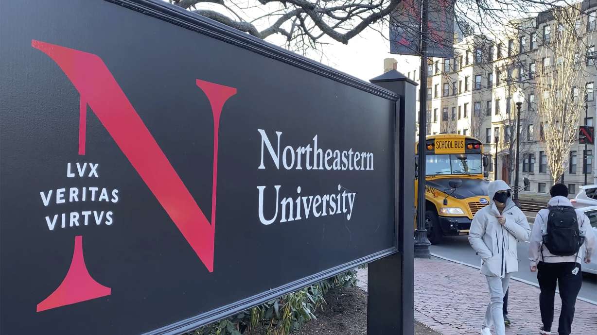 FILE - Pedestrians walk near a Northeastern University sign on the school's campus, Jan. 31, 2019, in Boston. Steve Waithe, a former college track and field coach at the university, could face seven years behind bars for setting up sham social media and email accounts in an attempt to trick women into sending him nude or semi-nude photos of themselves.