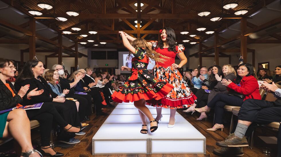 In a photo from the 2023 Fashion Show, two refugees show off their cultural dress on stage. The 2024 Fashion Show is being held on March 6, 2024, at the Zions Technology Center.