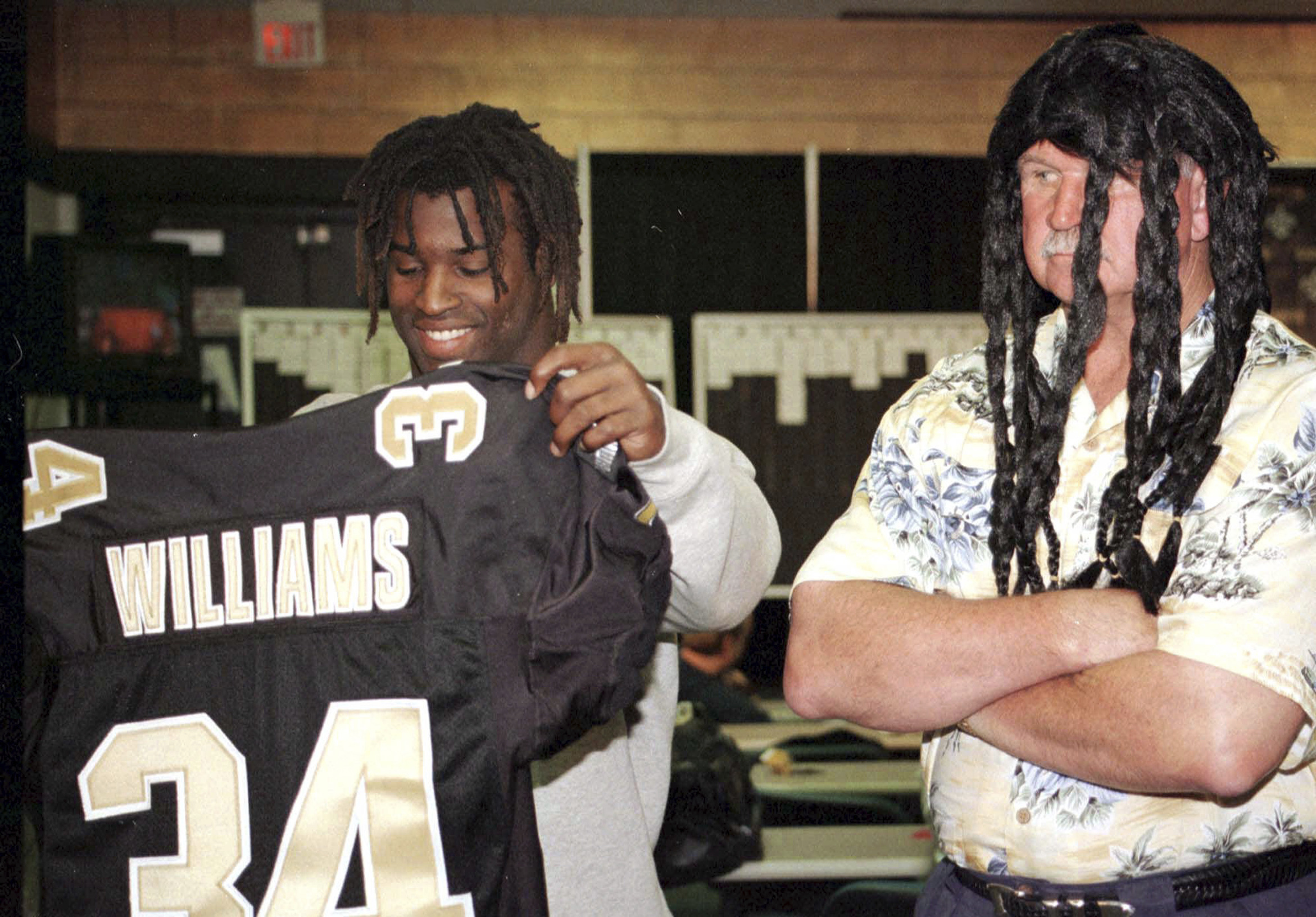 Then-New Orleans Saints first-round draft pick Ricky Williams checks out his New Orleans Saints jersey as coach Mike Ditka, wearing a dreadlock wig, looks on in Kenner, La., April 18, 1999. Ditka died on Friday at the age of 86.