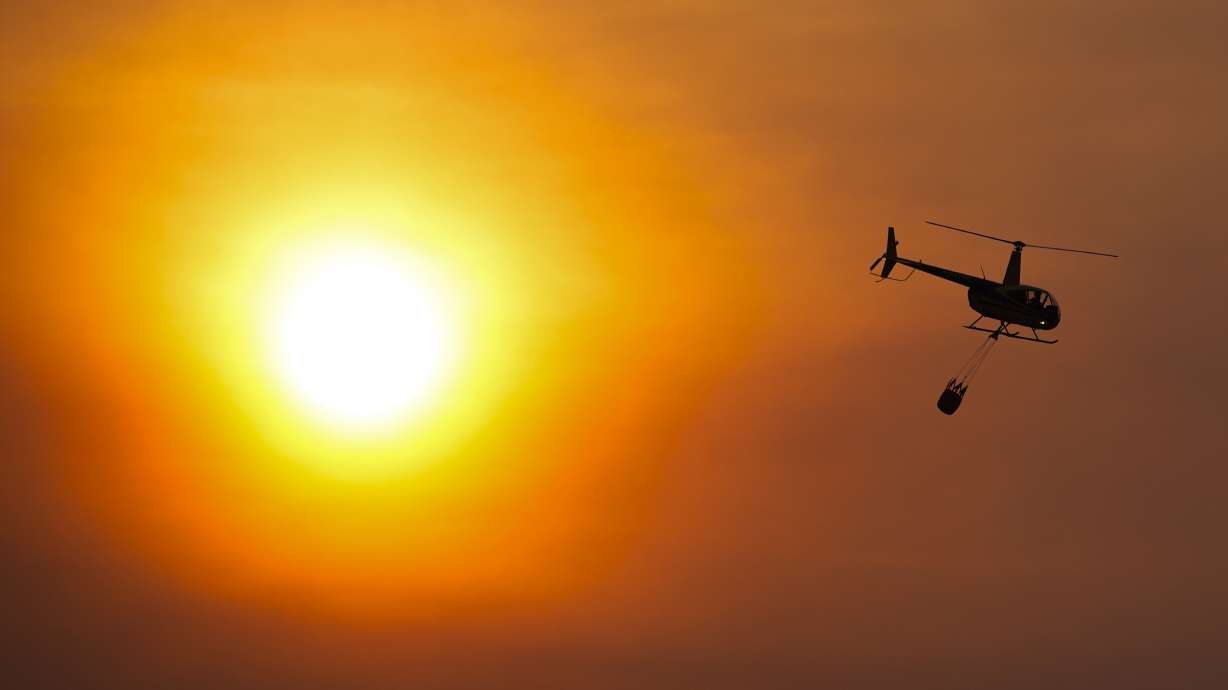 A helicopter carries a bucket as it flies over homes burned by the Smokehouse Creek Fire, Feb. 28, in Canadian, Texas. The utility provider Xcel Energy says Thursday its facilities appeared to have played a role in igniting a massive wildfire.