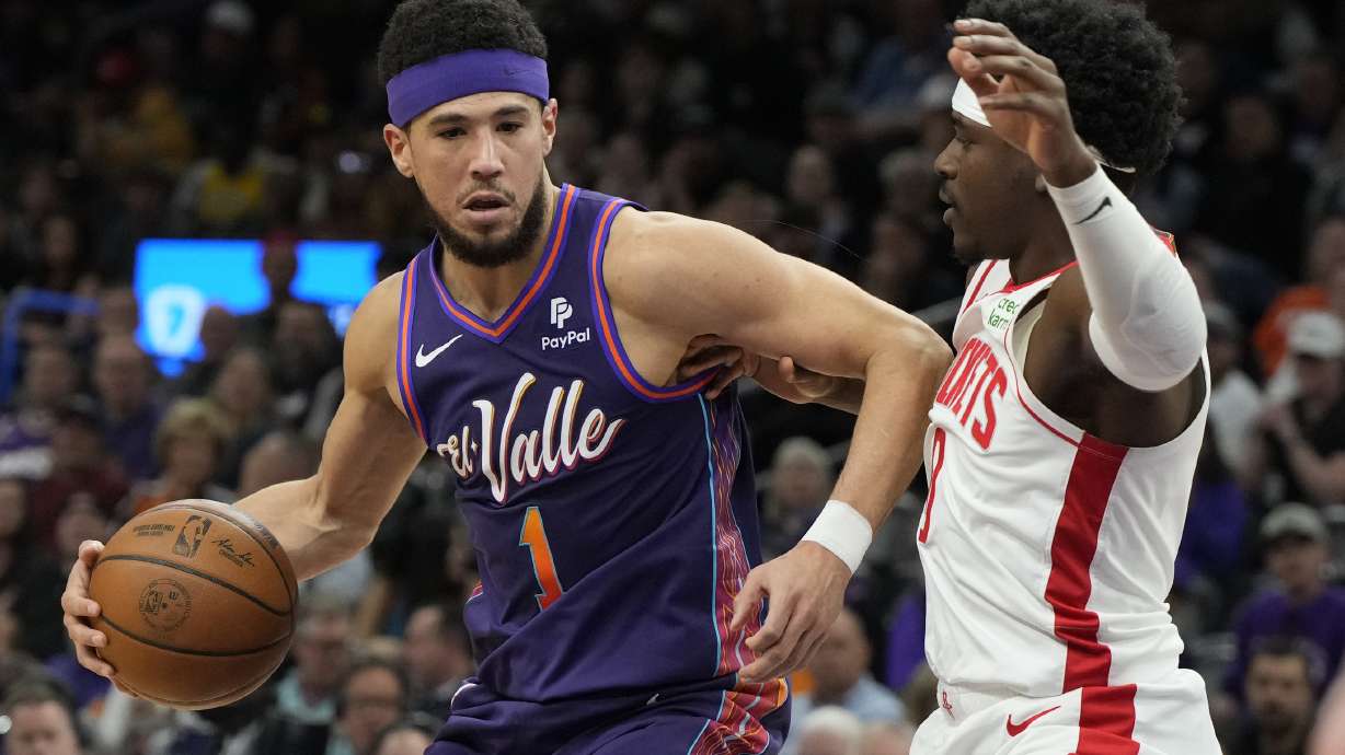 Phoenix Suns guard Devin Booker (1) drives against Houston Rockets guard Aaron Holiday, right, during the first half of an NBA basketball game, Thursday, Feb. 29, 2024, in Phoenix.