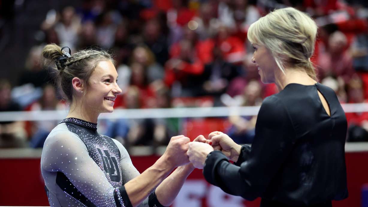 Utah Red Rocks’ Grace McCallum fist-bumps University of Utah gymnastics head coach Carly Dockendorf before competing on the beam during a gymnastics meet against Stanford and Utah State University at the Huntsman Center in Salt Lake City on Friday, March 15, 2024. The Utah Red Rocks won.