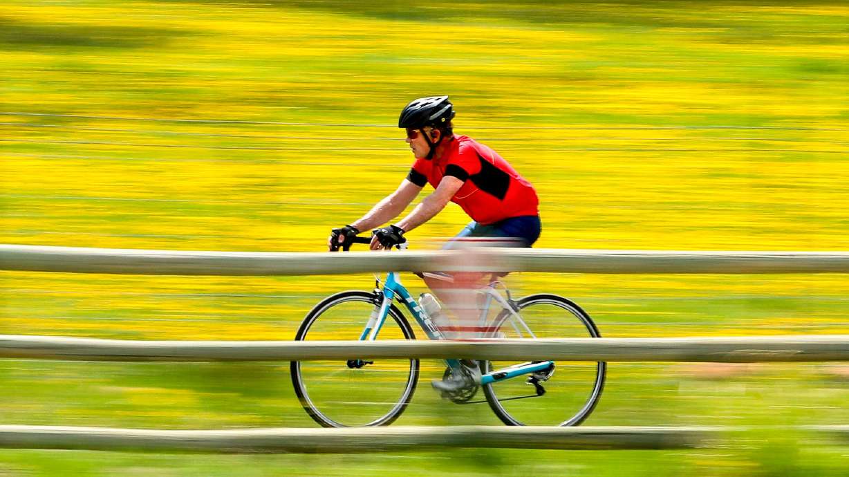 A biker zips past a field of dandelions while riding on the paved trail system in Park City on May 11, 2020. The Biden administration has a new grant program that authorizes connecting existing trails.