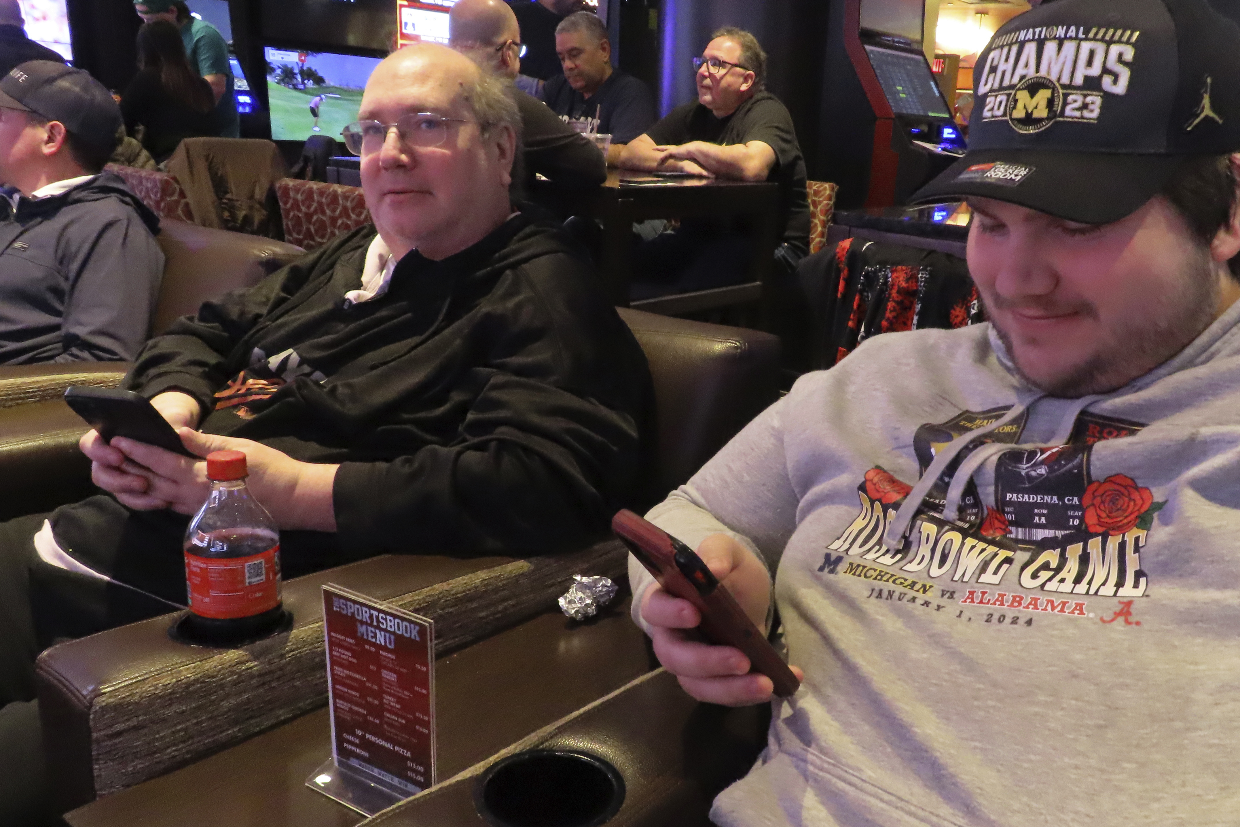 Mark F. Bawers, left, and his won Mark A. Bawers, right, check their phones while waiting for the NCAA basketball tournament to begin as they sit in the sports book at Golden Nugget casino in Atlantic City N.J. on Wednesday, March 21, 2024. The American Gaming Association estimates Americans will wager $2.72 billion with legal outlets this year. 
