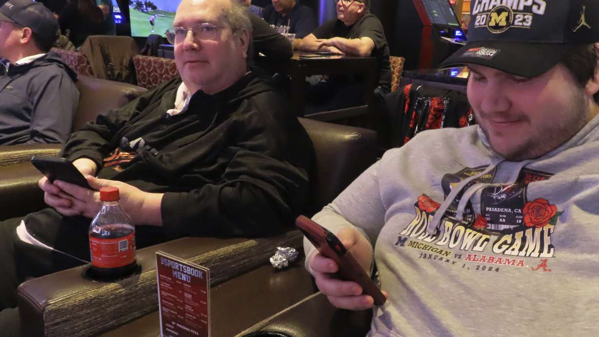 Mark F. Bawers, left, and his won Mark A. Bawers, right, check their phones while waiting for the NCAA basketball tournament to begin as they sit in the sports book at Golden Nugget casino in Atlantic City N.J. on Wednesday, March 21, 2024. The American Gaming Association estimates Americans will wager $2.72 billion with legal outlets this year.