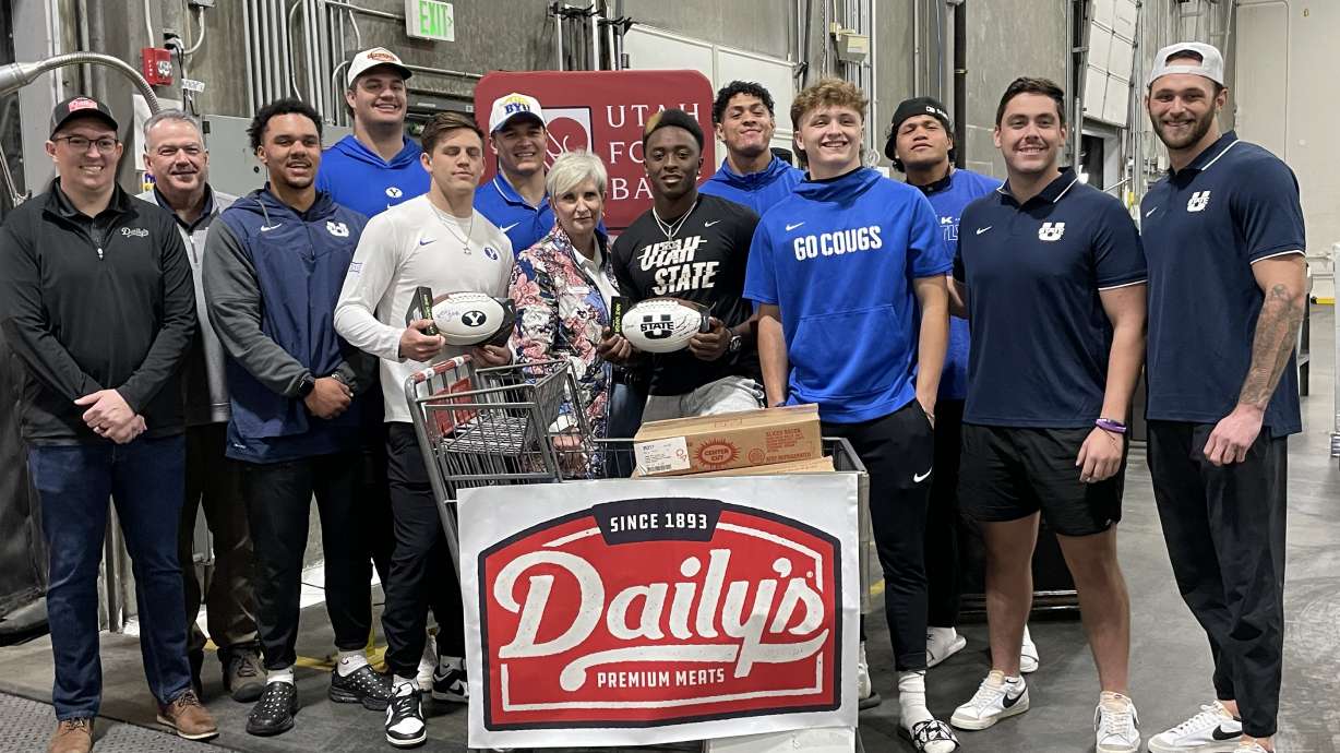 Ginette Bott stands with USU and BYU football players for a photo celebrating the donation of pork made through the Protein for Points fundraising initiative on Thursday.