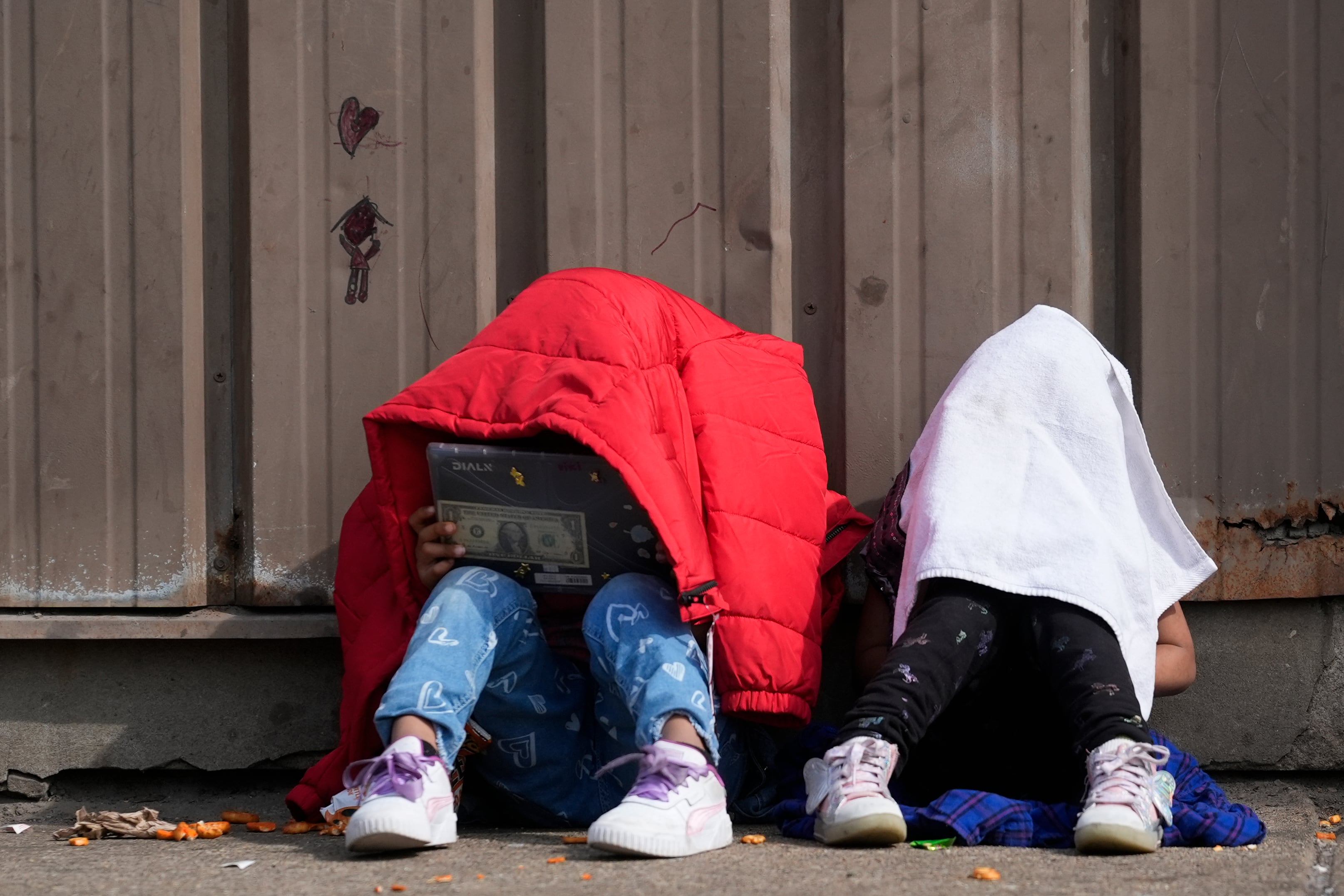 Children cover their heads as they sit outside of a migrant shelter March 13, in the Pilsen neighborhood of Chicago. Multiple people living at the shelter for migrants have tested positive for measles since last week. A team from the Centers for Disease Control and Prevention is supporting local officials' response.