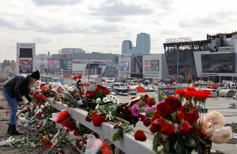 A woman lays flowers on the roadside in front of the burnt-out Crocus City Hall following a deadly attack on the concert venue on the outskirts of Moscow, Russia, Tuesday.