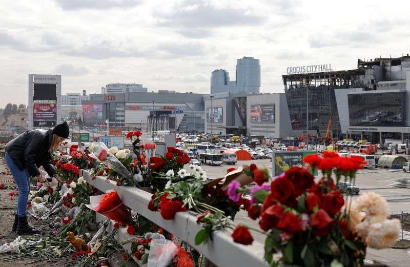 A woman lays flowers on the roadside in front of the burnt-out Crocus City Hall following a deadly attack on the concert venue on the outskirts of Moscow, Russia, Tuesday.