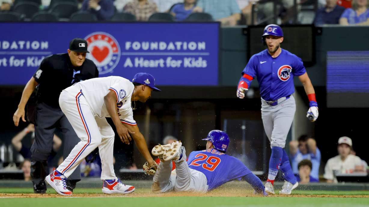 Chicago Cubs' Michael Busch (29) scores on a wild pitch as Texas Rangers pitcher José Leclerc, left, attempts the tag during the ninth inning of a baseball game Thursday, March 28, 2024 in Arlington, Texas.