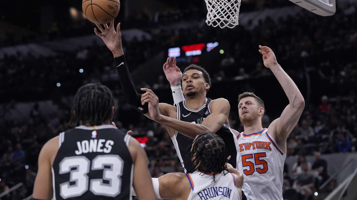 San Antonio Spurs center Victor Wembanyama, center, passes the ball over New York Knicks guard Jalen Brunson (11) during the second half of an NBA basketball game in San Antonio, Friday, March 29, 2024.
