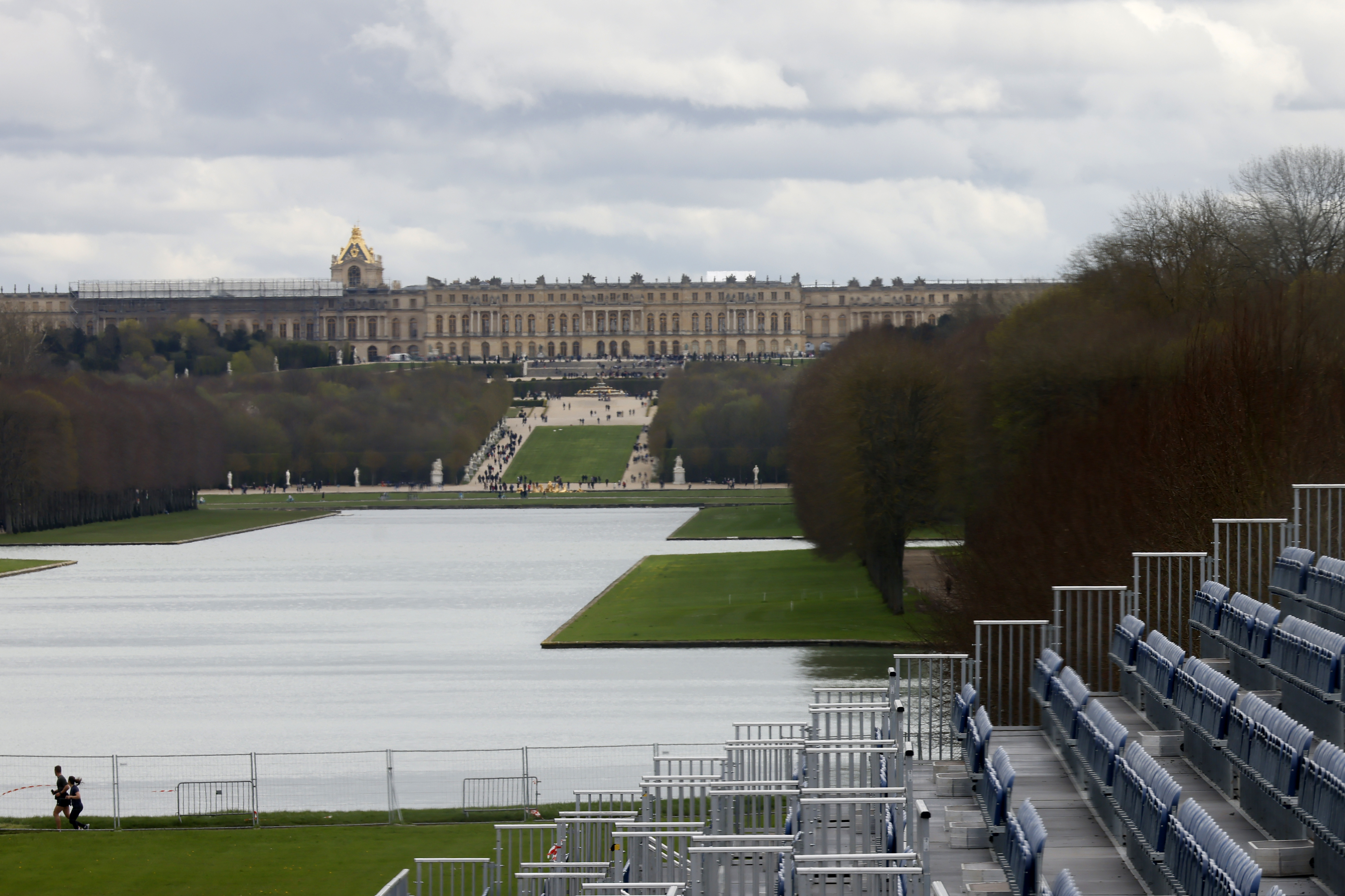 A couple jogs past the stands to watch the equestrian sports, Friday, March 29, 2024 in the park of the Chateau de Versailles, west of Paris. The site will be the venue for equestrian sports at the Paris 2024 Olympic Games. The Chateau de Versailles is seen in background. 