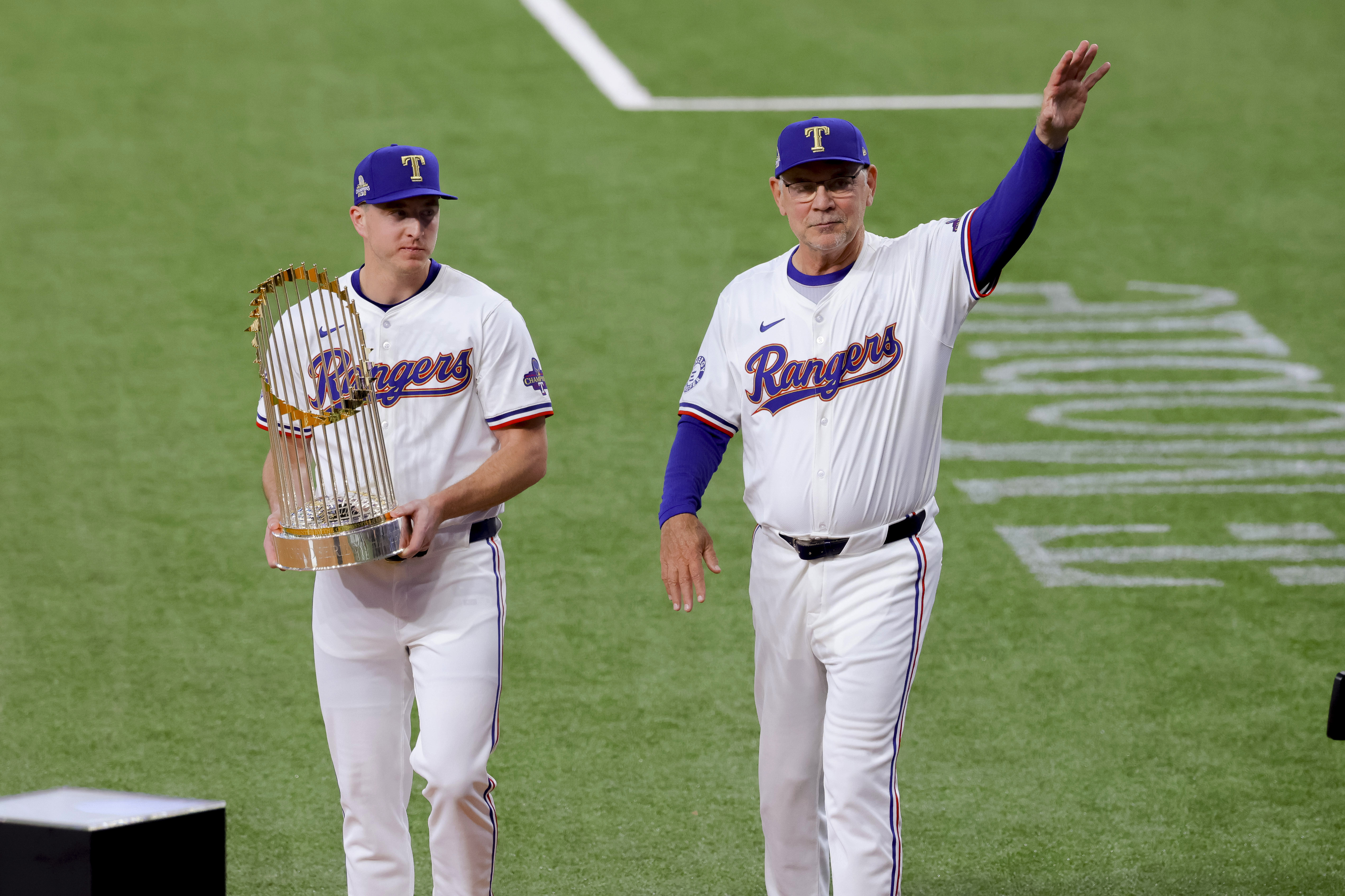 Texas Rangers relief pitcher Josh Sborz, left, and manager Bruce Bochy, right, walk the Commissioner's Trophy onto the field before the team's baseball game against the Chicago Cubs, Thursday, March 28, 2024 in Arlington, Texas. 
