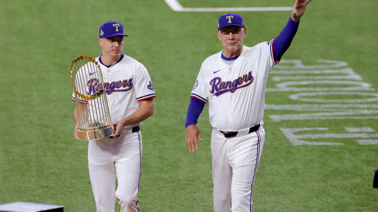 Texas Rangers relief pitcher Josh Sborz, left, and manager Bruce Bochy, right, walk the Commissioner's Trophy onto the field before the team's baseball game against the Chicago Cubs, Thursday, March 28, 2024 in Arlington, Texas.