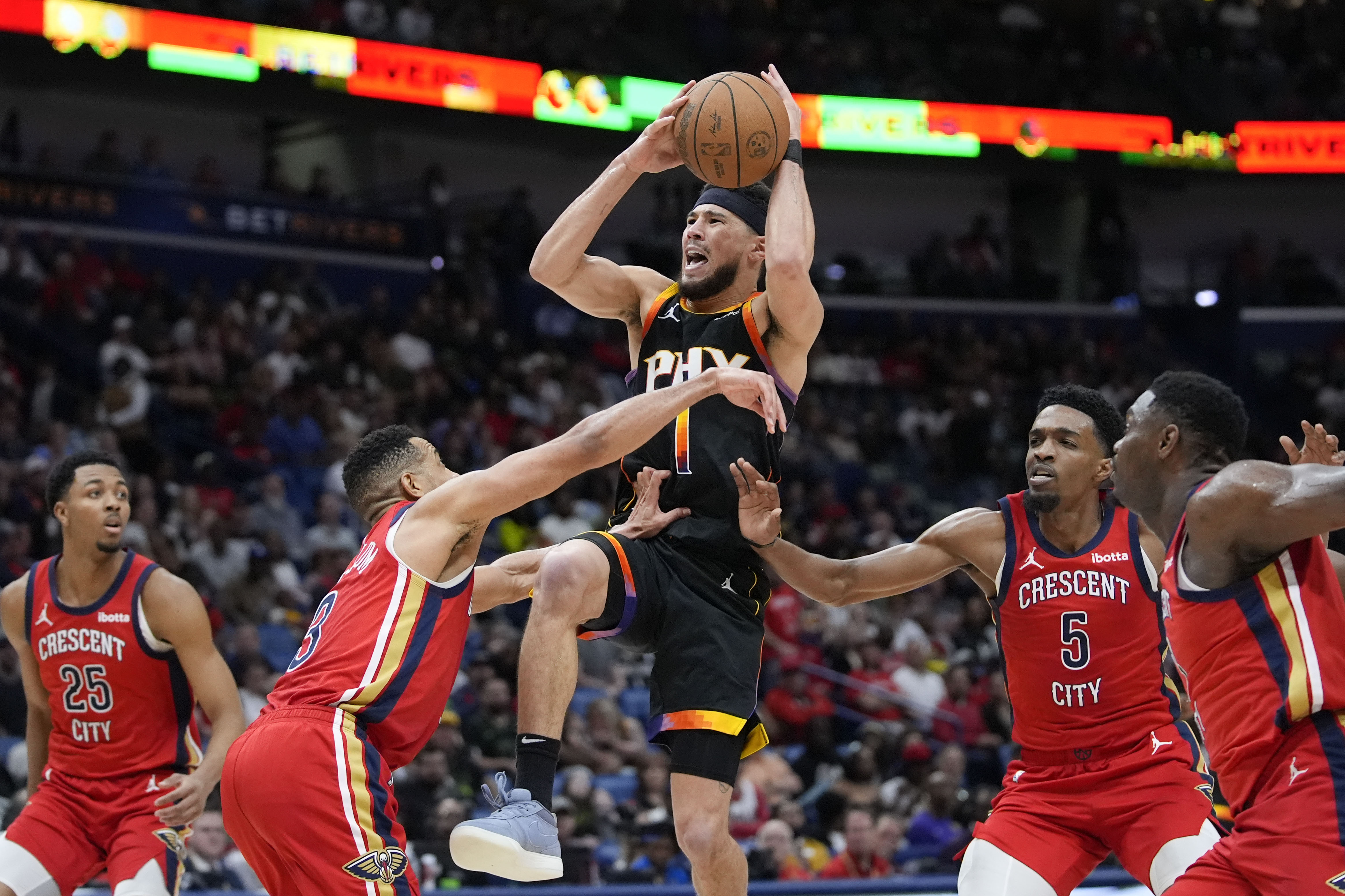 Phoenix Suns guard Devin Booker (1) goes to the basket between New Orleans Pelicans guard CJ McCollum (3) and forward Herbert Jones (5) in the second half of an NBA basketball game in New Orleans, Monday, April 1, 2024. The Suns won 124-111. 