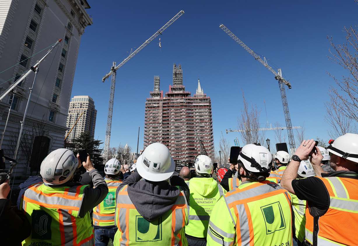 Photos are taken by construction workers as the Angel Moroni is raised atop the Salt Lake Temple in Salt Lake City on Tuesday, April 2, 2024.