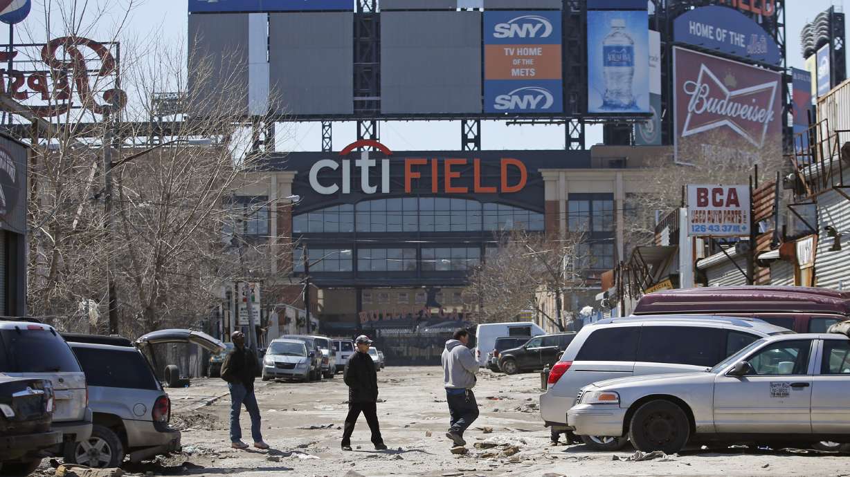 FILE - In this April 2, 2015 photo, workers cross an unpaved street adjacent to Citi Field, home to the New York Mets baseball team in the Willets Point section of the Queens borough of New York. New York City officials approved a plan Thursday, April 11, 2024, to build a 25,000-seat stadium for Major League Soccer’s New York City Football Club next to the New York Mets’ stadium, Citi Field. The $780 million soccer stadium, expected to open in 2027, will anchor a 23-acre redevelopment project in the neighborhood known as Willets Point that will also include housing, a new public school, retail stores and a hotel.