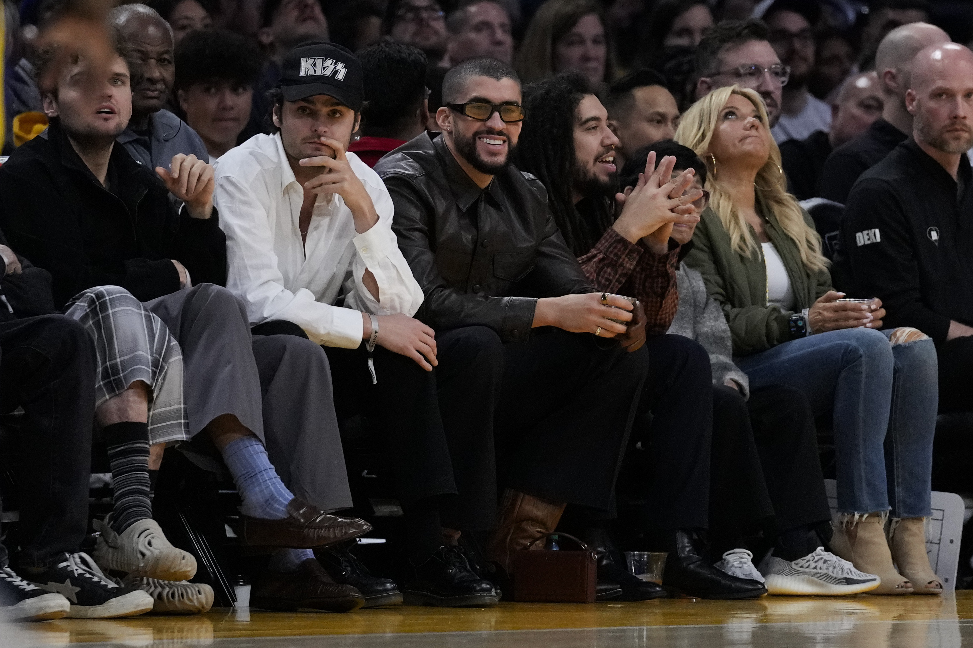 Bad Bunny, center, watches the second half of an NBA basketball game between the Golden State Warriors and the Los Angeles Lakers in Los Angeles, Saturday, March 16, 2024. 