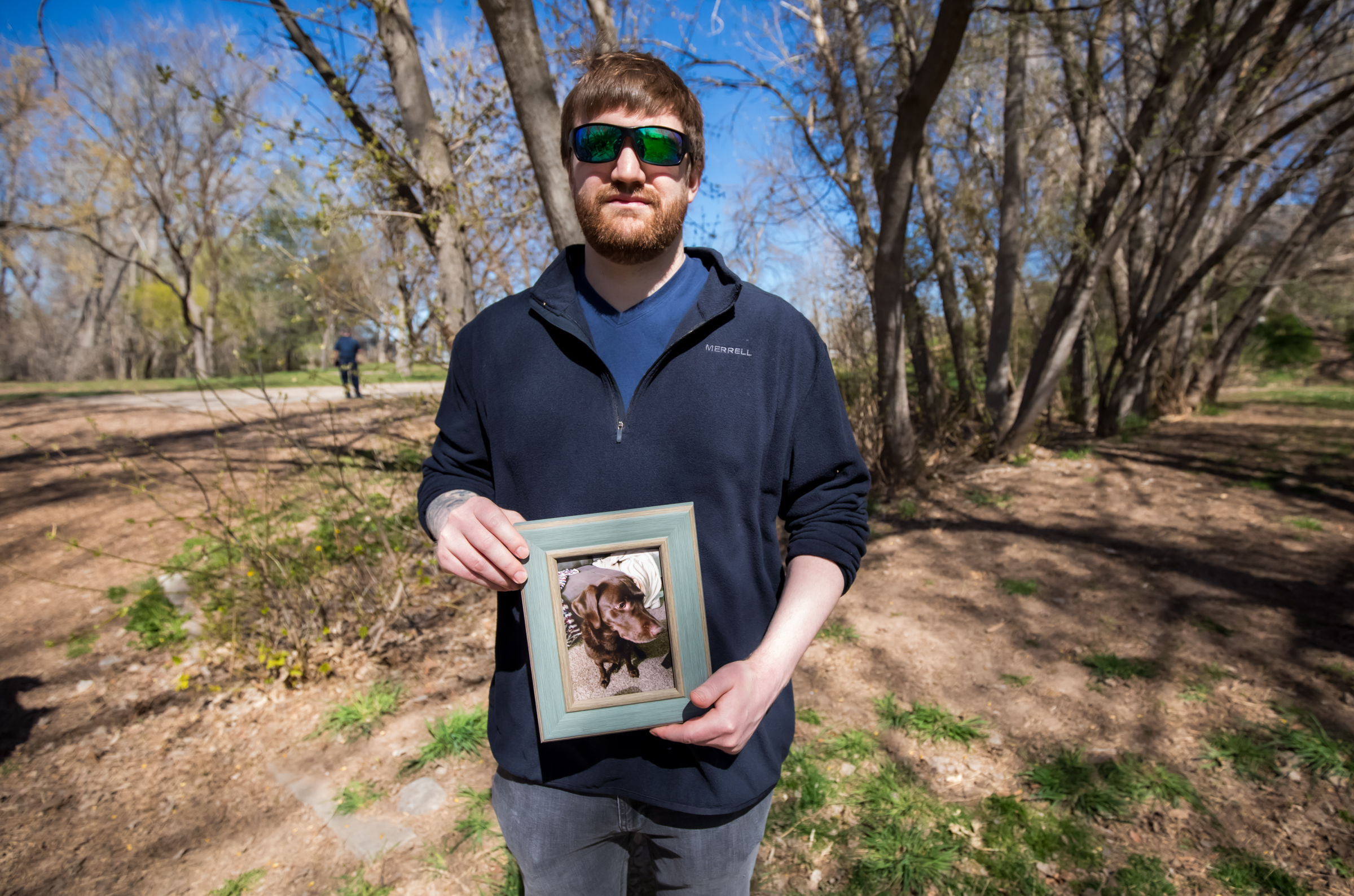 Travis Mundt, of West Jordan, poses with a framed photo of his dog Oliver at Sugar House Park on Friday. Oliver was swept away in Parleys Creek last year and never found.