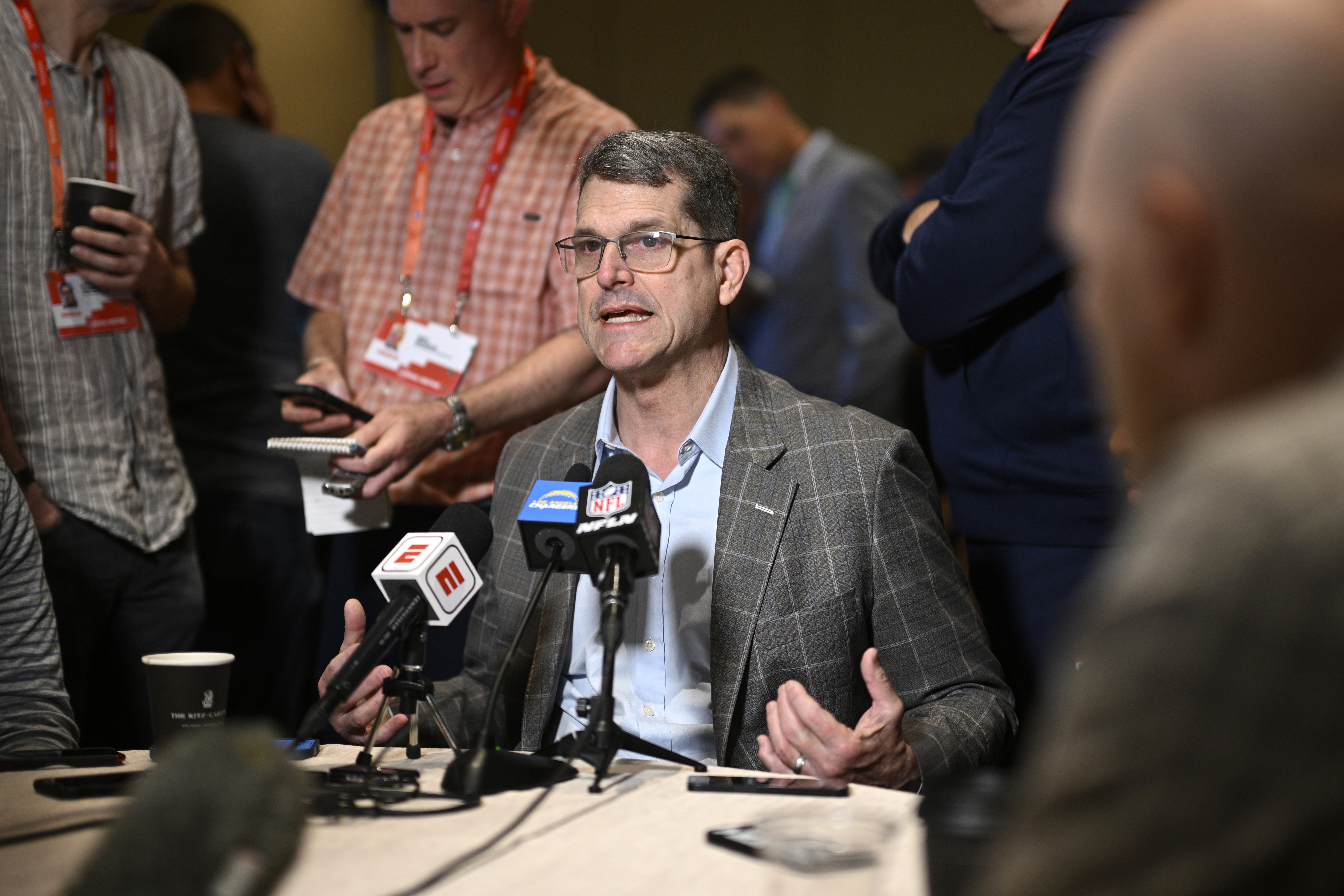 FILE - Los Angeles Chargers head coach Jim Harbaugh, center, talks with reporters during an AFC coaches availability at the NFL football owners meetings, Monday, March 25, 2024, in Orlando, Fla. Michigan was given three years of probation, fined and hit with recruiting limits by the NCAA on Tuesday, April 16, after football coaches and staff had impermissible contact with recruits and players under coach Jim Harbaugh while access was restricted during the COVID-19 pandemic.