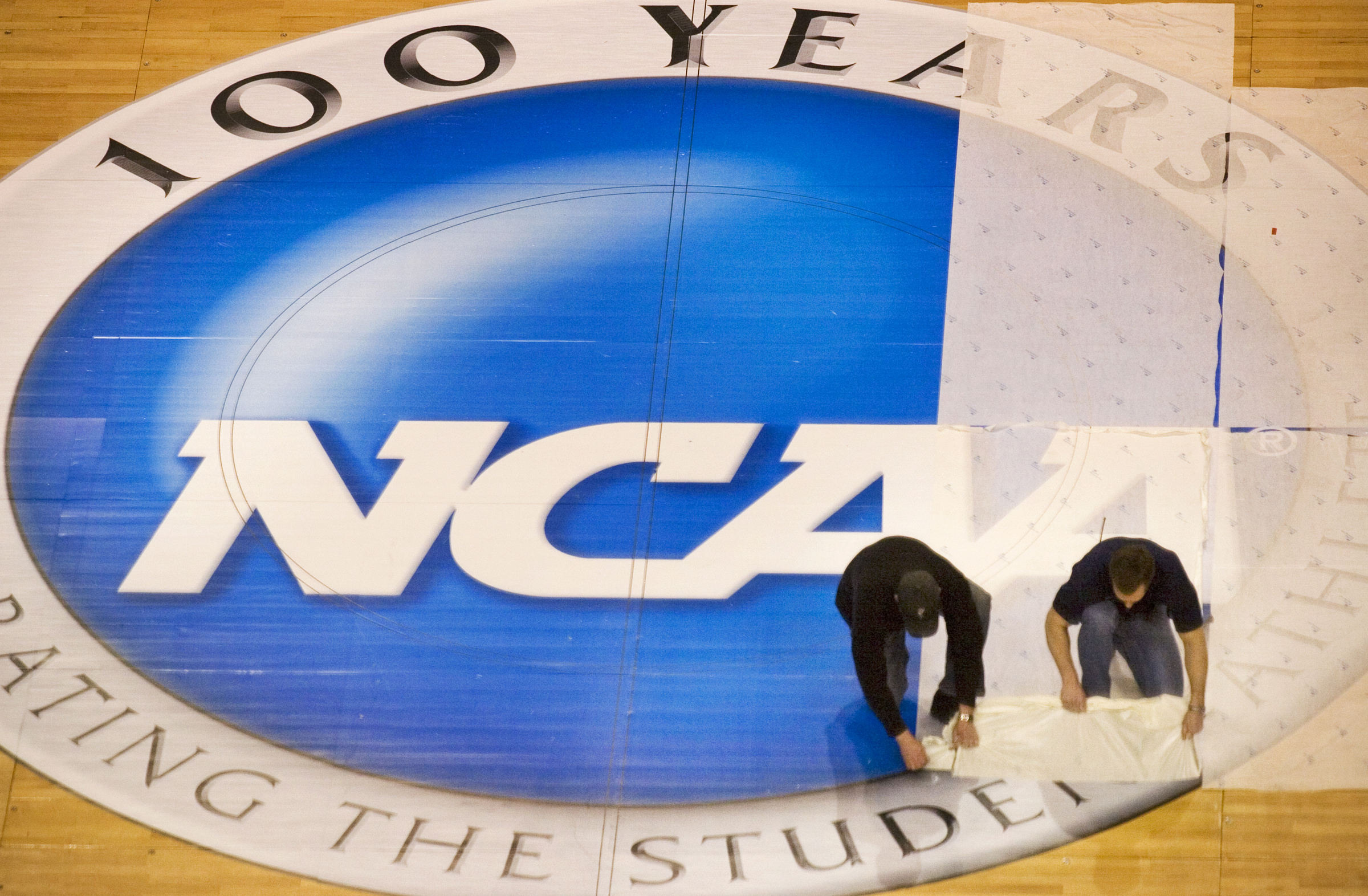 FILE - Wachovia Center operations manager Jim McDonald, left, and carpenter foreman Tim Allen remove the protective film covering the NCAA logo at mid-court on the center's basketball court, Wednesday, March 15, 2006, in Philadelphia. NCAA athletes will be immediately eligible to play no matter how many times they transfer — as long as they meet academic requirements — after the association fast-tracked legislation Wednesday, April 17, 2024, to fall in line with a recent court order. 