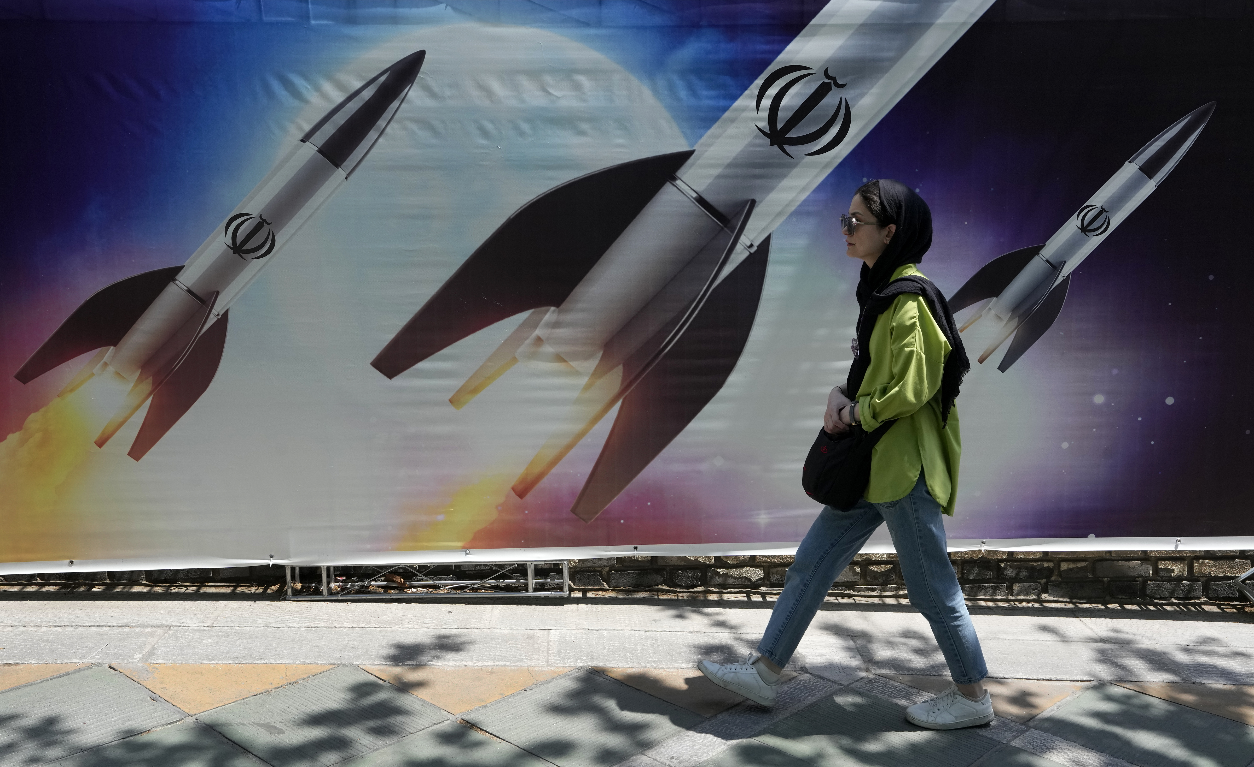 A woman walks past a banner showing missiles being launched, in northern Tehran, Iran, Friday.