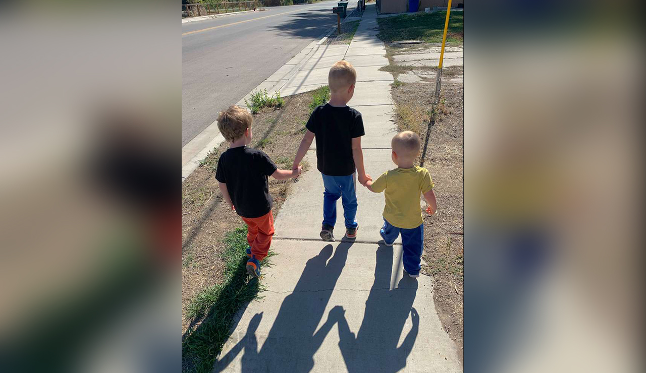 The three boys walking down a sidewalk together, holding hands.