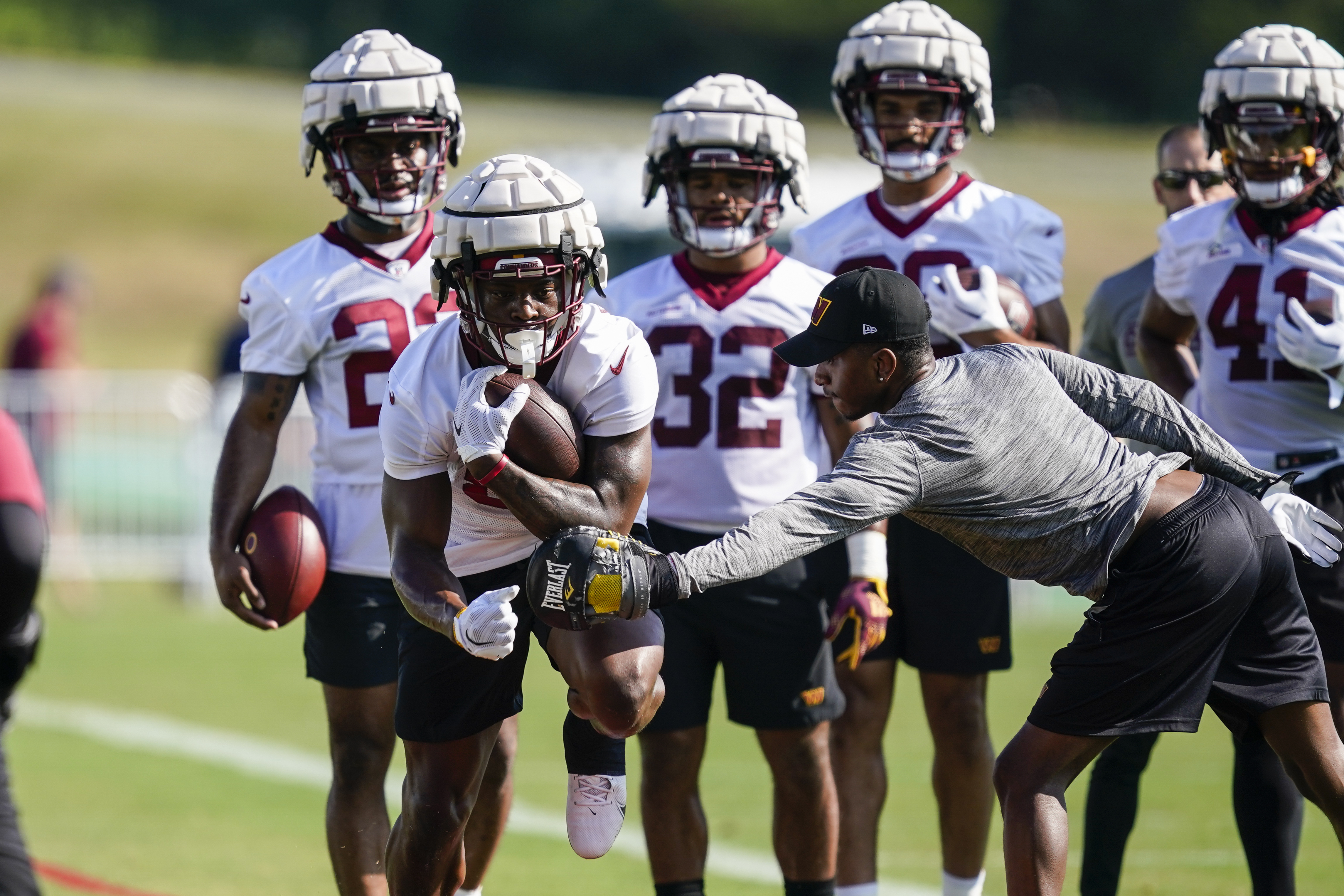 FILE - Washington Commanders running back Brian Robinson, second from left, wears a Guardian cap during practice at the team's NFL football training facility July 27, 2022 in Ashburn, Va. The NFL says will allow players to wear protective soft-shell helmet covers known as Guardian caps during games next season if they choose. The league is also expanding the use of the devices during practices. Defensive backs and receivers have joined the position groups now required to wear the caps during all contact practices.