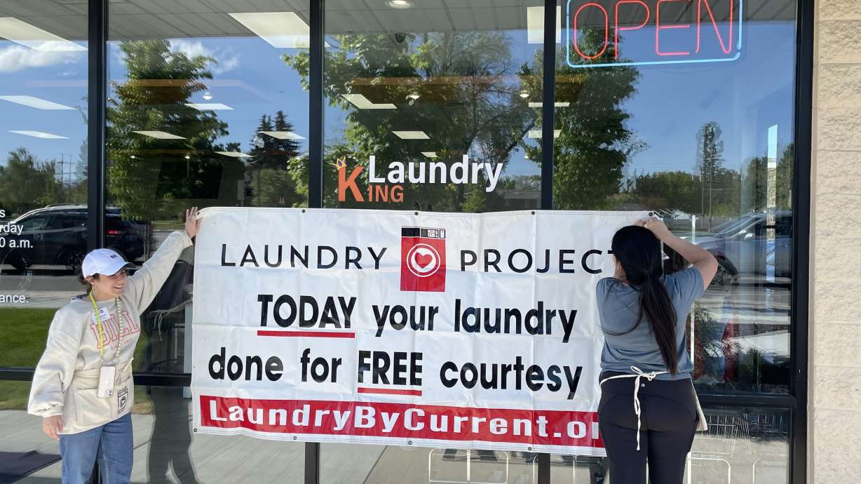 Volunteers hang a banner advertising the Laundry Project initiative at a laundromat in West Valley City on Wednesday.