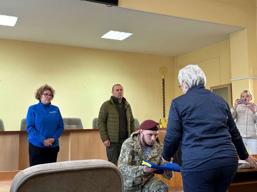 Senior Sergeant Baidukov Yaroslav, center, presented a flag signed by soldiers fighting on the front line in Zaporozhye to Terri Hepworth, right, in this undated photo.