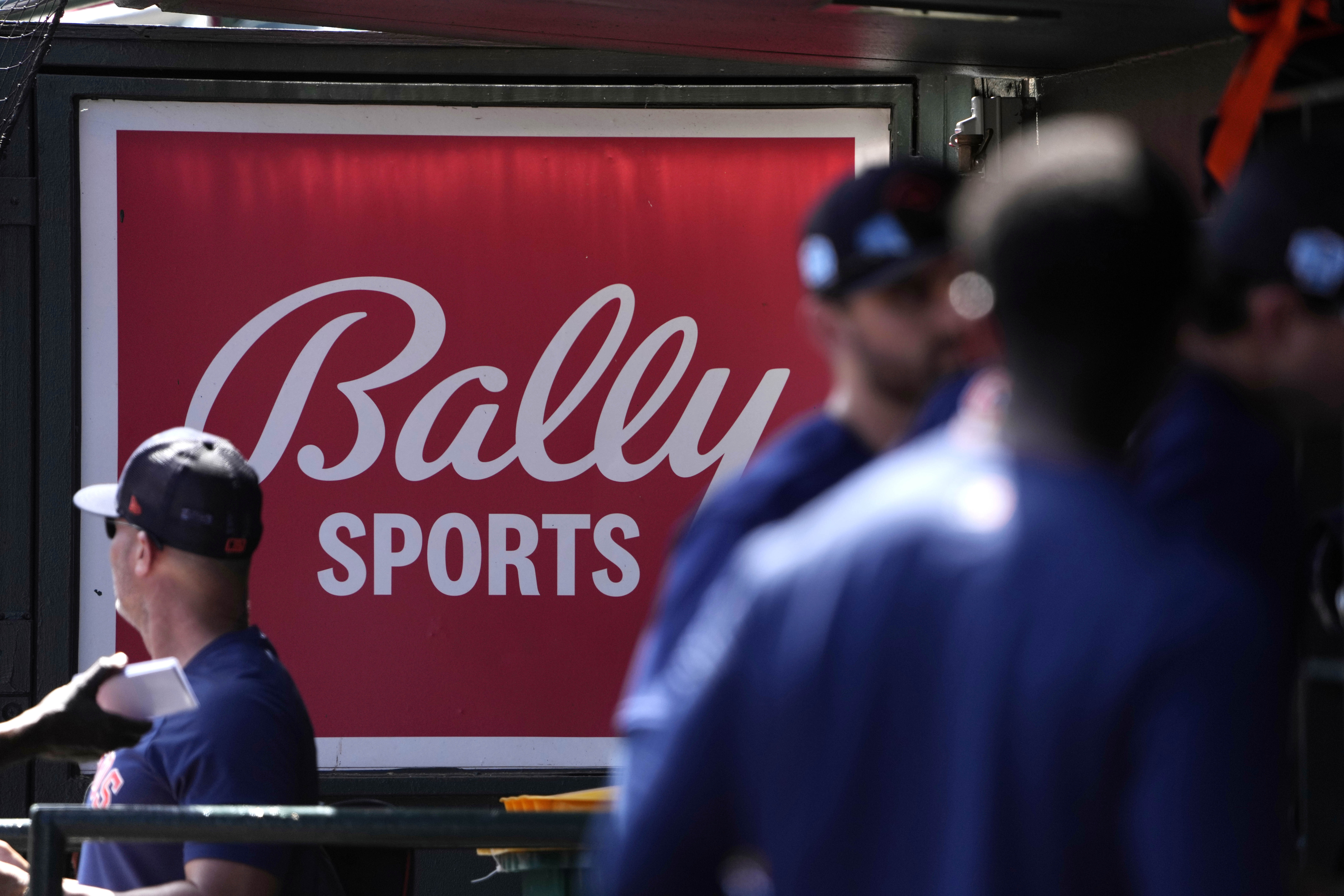 FILE -A Bally Sports sign hangs in a dugout before the start of a spring training baseball game between the St. Louis Cardinals and Houston Astros Thursday, March 2, 2023, in Jupiter, Fla. Comcast has blacked out 15 regional sports networks offered by Bally Sports, escalating a contract dispute with their distributor. The cutoff that began Wednesday, May 1, 2024 affects games played by a dozen Major League Baseball teams based in nine states. 