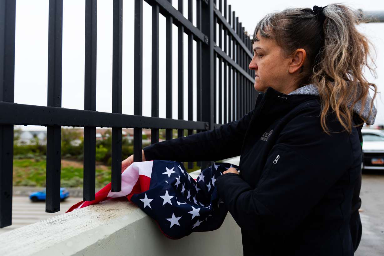 Kathy Harkin hangs an American flag over I-15 as a procession with the body of a fallen Santaquin police officer drives by at an overpass at 10600 South in Sandy on Monday.