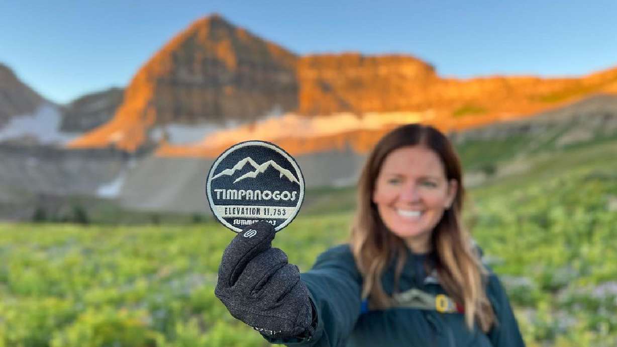 A woman holds a 2023 Timp Badge in front of Provo's Mount Timpanogos. Timpanogos Hiking Co. revived an old tradition of handing out badges to anyone who summits the mountain.