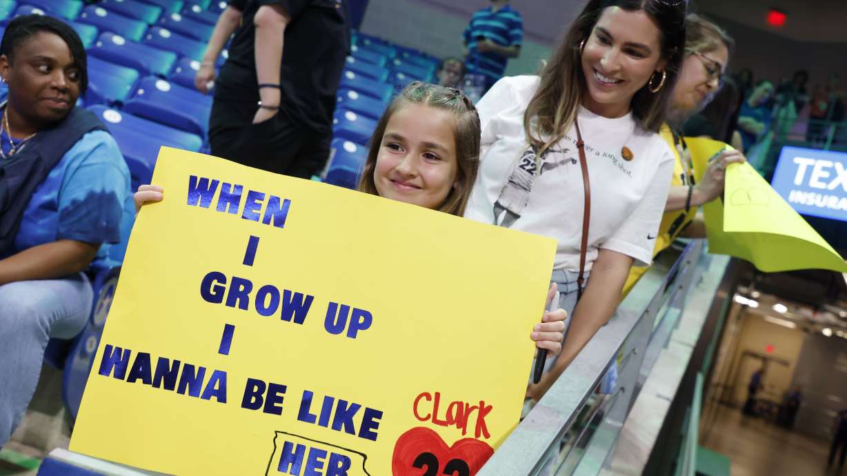 CORRECTS FROM CAITLYN TO CAITLIN - Pailynn Amos, center, holds a sign for Indiana Fever guard Caitlin Clark in front of her mother Rebecca Amos, of Ennis, Texas, prior to an WNBA basketball game against the Dallas Wings in Arlington, Texas, Friday, May 3, 2024.