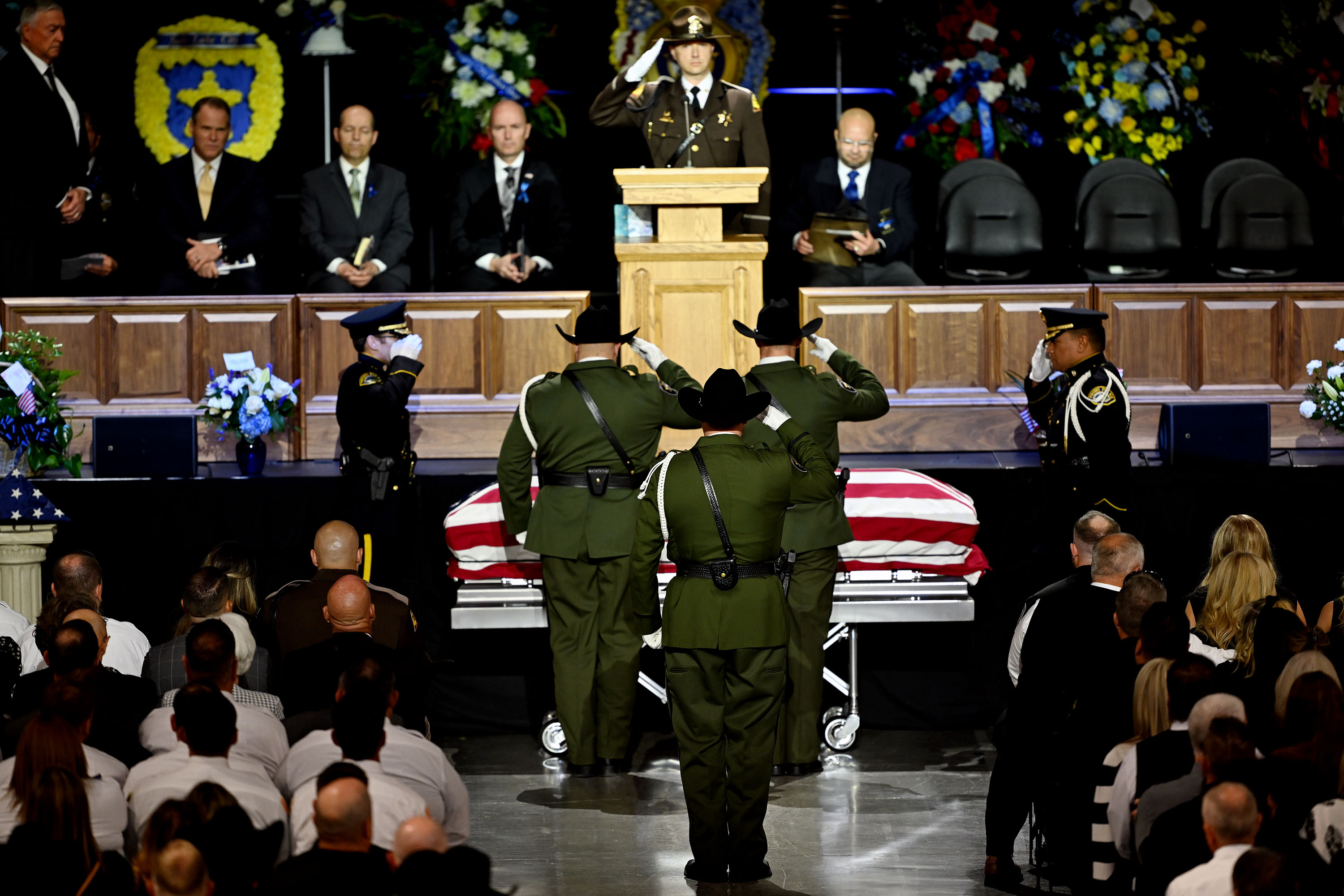 Officers salute as the casket is brought in for funeral services for Santaquin Police Sgt. Bill Hooser in the UCCU Center at UVU in Orem on Monday.