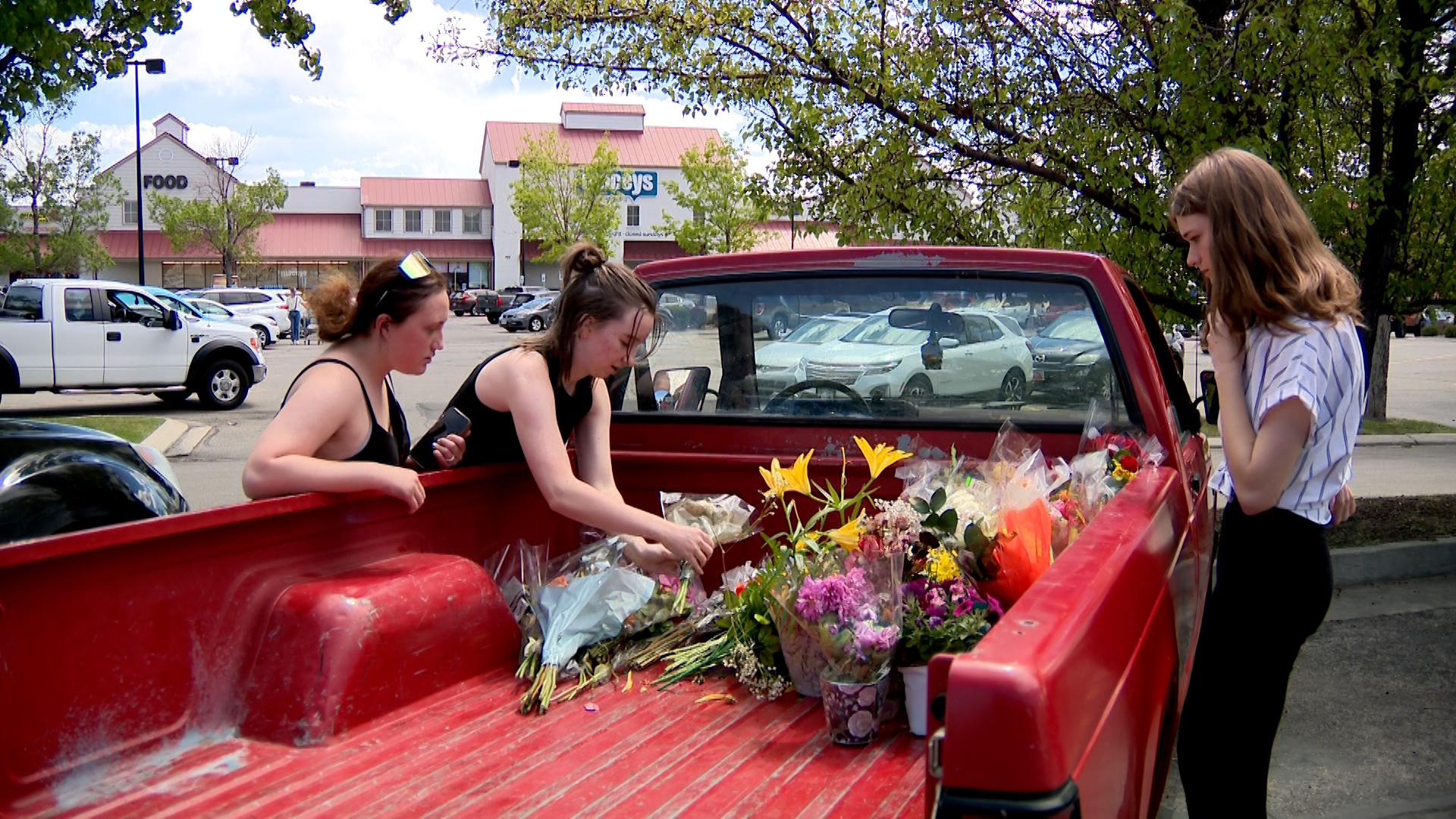 Three Lehi High School students get flowers out of a truck bed to support the teacher who was hurt.