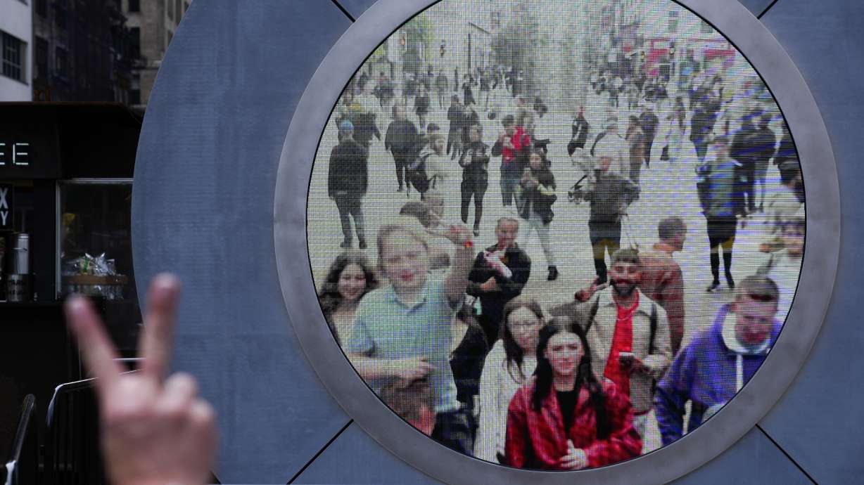 People in both New York and Dublin, Ireland, wave and signal at each other while looking at a livestream view of one another as part of an art installation on the street in New York, May 14.