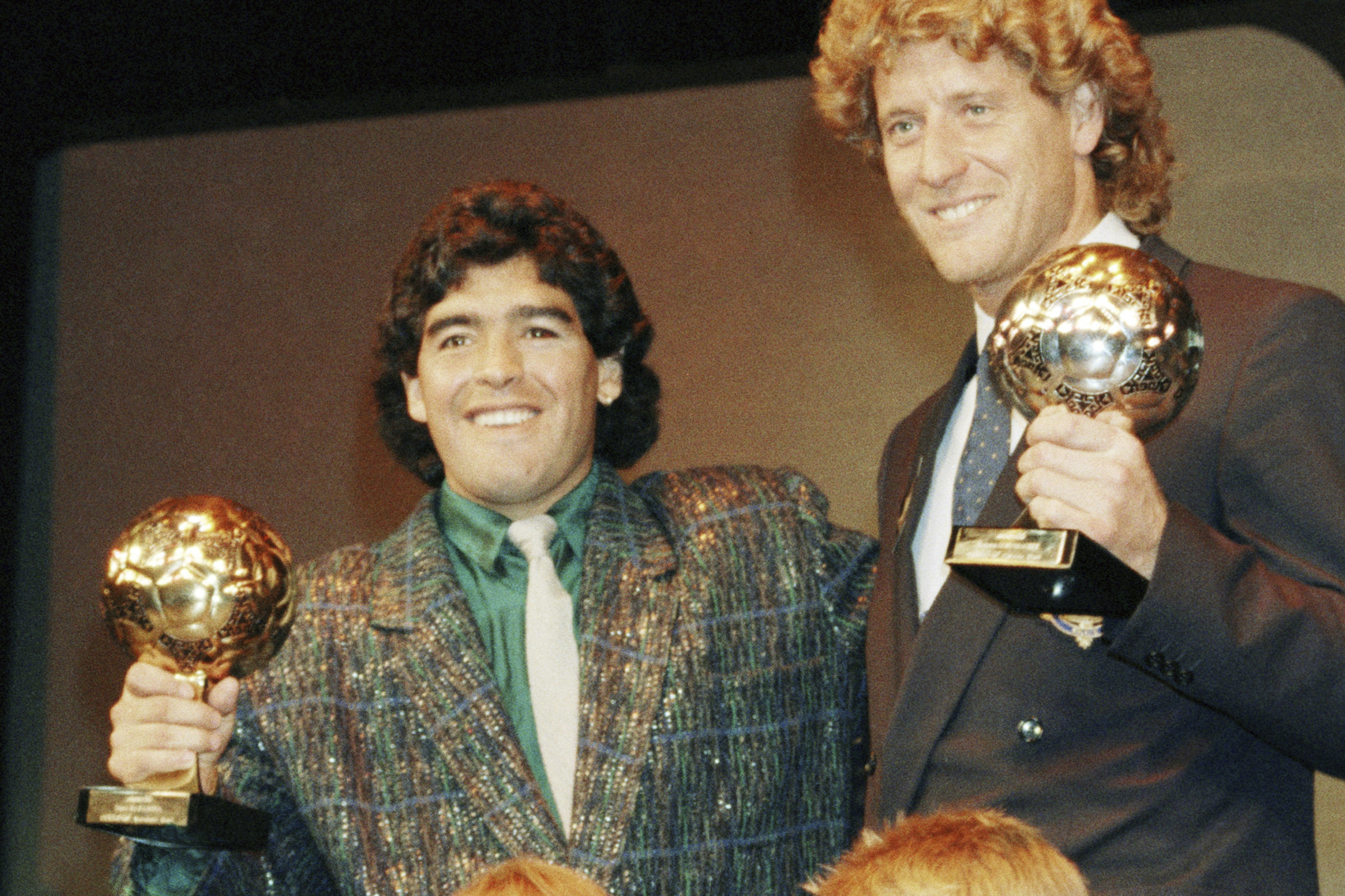 FILE - Argentina's soccer star Diego Maradona, left, and West German goalkeeper Harald Schumacher are holding their World Cup Soccer Ball awards while posing with two young soccer players during the Soccer Golden Shoe Award ceremony held in Paris, France, on Nov. 13, 1986. Diego Maradona's heirs filed a lawsuit to try to stop the auction of a trophy he was awarded after the 1986 World Cup won by Argentina.