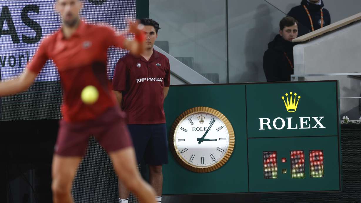Serbia's Novak Djokovic plays a shot against Italy's Lorenzo Musetti as the clock indicates the match time played in the fifth set of their third round match of the French Open tennis tournament at the Roland Garros stadium in Paris, Sunday, June 2, 2024.
