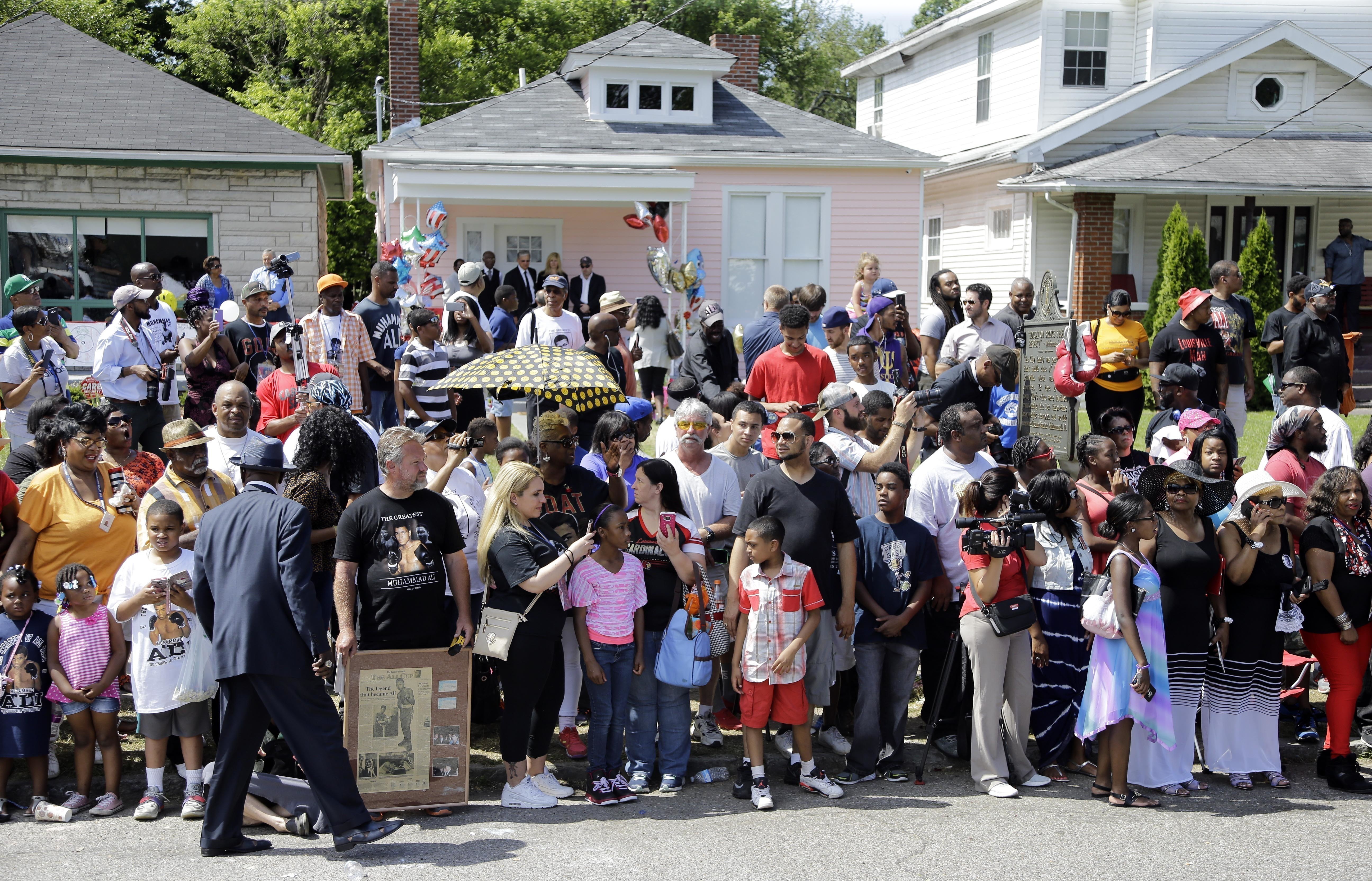 FILE - In this June 10, 2016, file photo, people line the street in front of the boyhood home, center with the pink wall, of Muhammad Ali as they wait for Ali's funeral procession to arrive in Louisville, Ky. The house where Ali grew up dreaming of boxing fame is up for sale. The house was converted into a museum offering a glimpse into the boxing great's formative years. It went on the market Tuesday, June 4, 2024 along with two neighboring homes. 