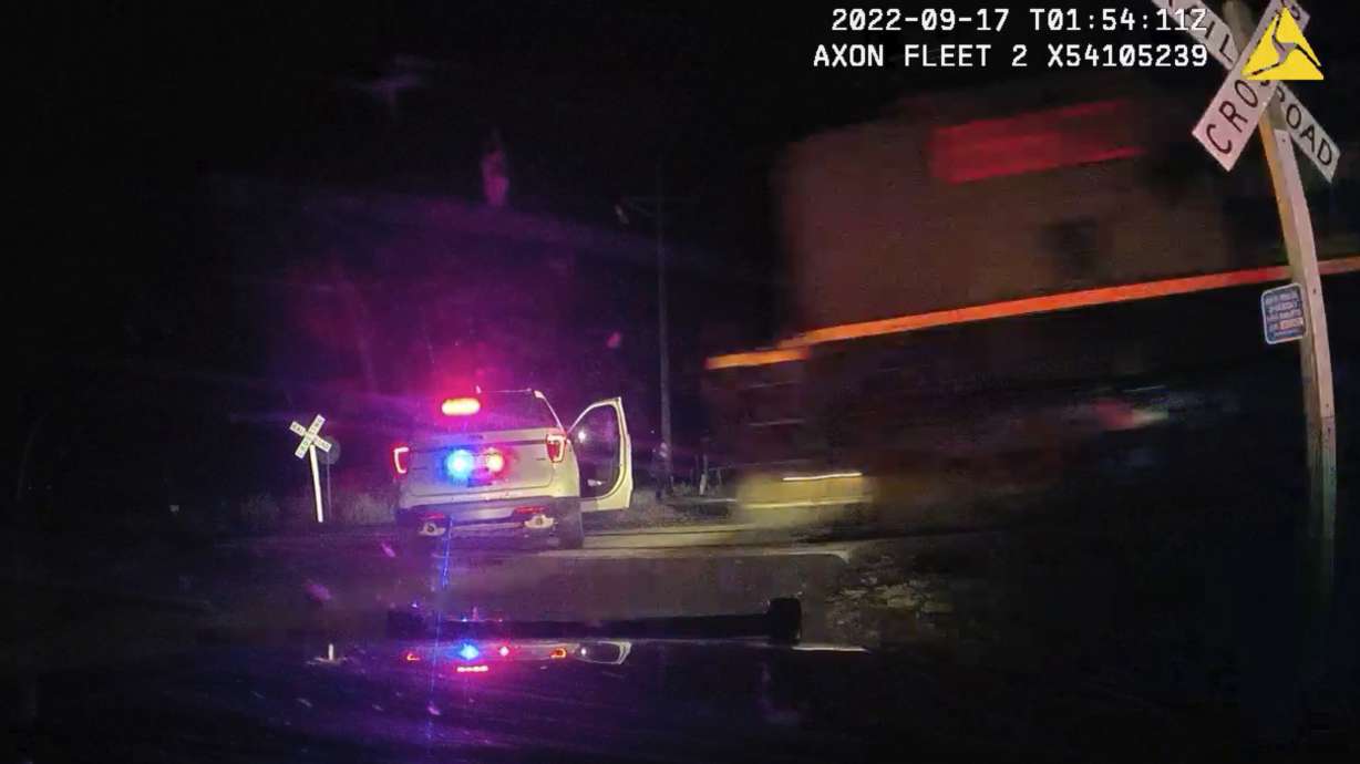 This dash camera image shows a train barreling toward a parked police car with a suspect inside, Sept. 16, 2022, in Fort Lupton, Colo. A city and town has agreed to pay $8.5 million settlement with the woman in the police car.