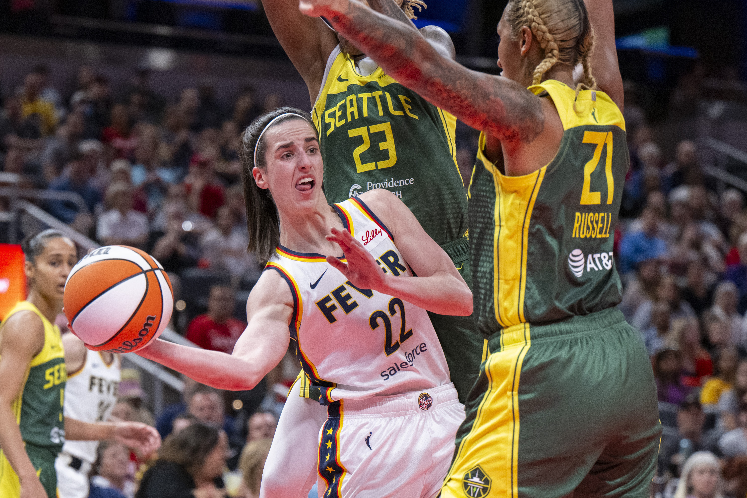 FILE - Indiana Fever guard Caitlin Clark (22) passes the ball from under the basket while being defended by Seattle Storm guard Jordan Horston (23) and center Mercedes Russell (21) during the first half of a WNBA basketball game Thursday, May 30, 2024, in Indianapolis. 