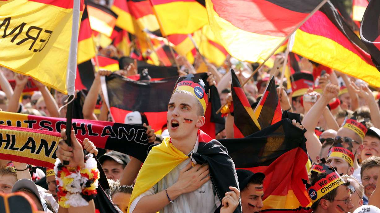 FILE - A German soccer fan sings the German national anthem prior to the beginning of the Round of 16 of the World Cup soccer match Germany against Sweden at the public viewing area where fans could watch the match live from Munich, on a giant television screen in Berlin, Saturday, June 24, 2006. Germany gets the 2024 European Championship underway against Scotland in Munich on Friday. However, away from the stadiums and public-viewing areas, few German flags are flying. Germany's dark history, rising far-right cast shadow on national pride before it hosts Euro 2024.